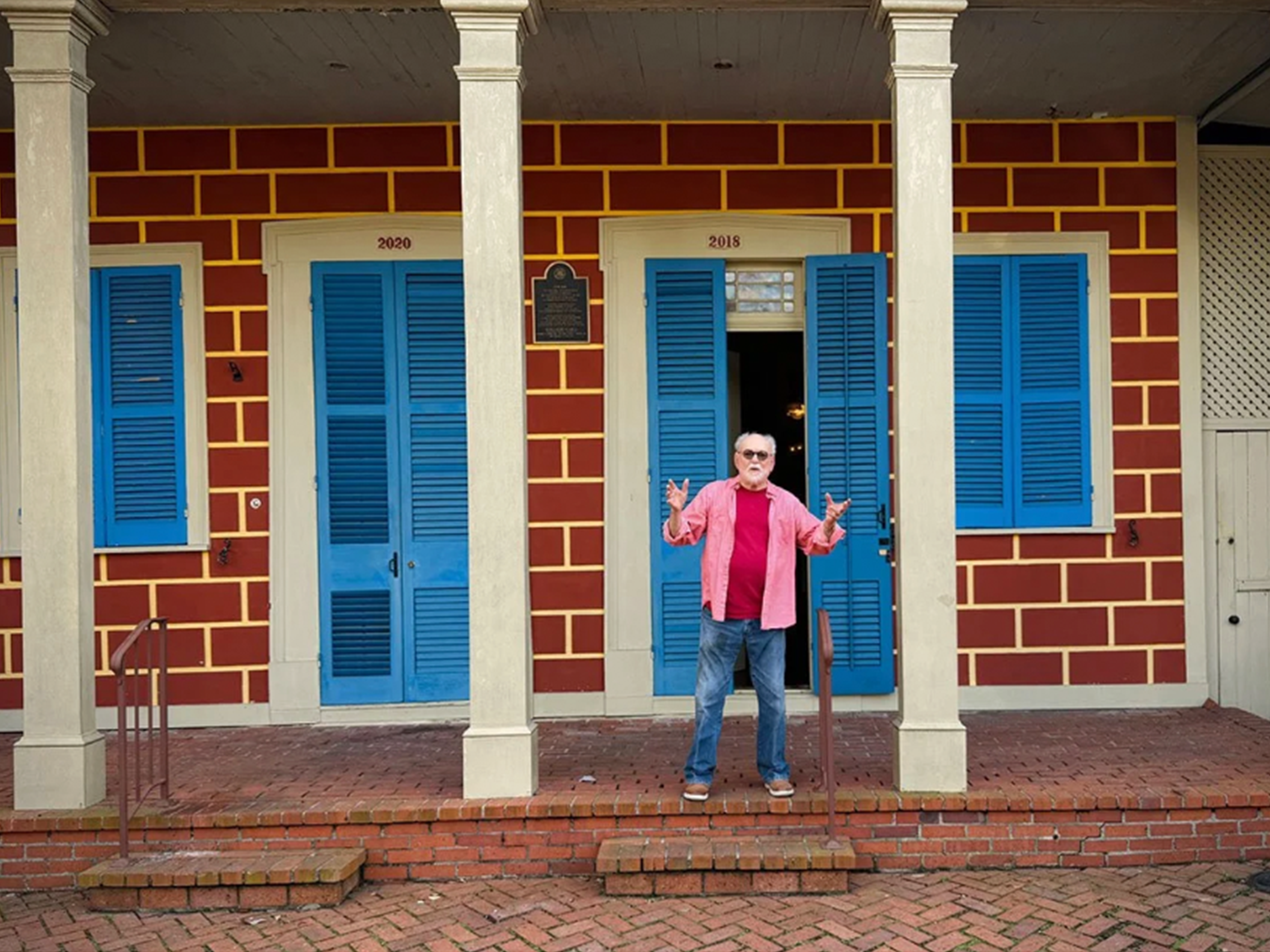 Gene Cizek on the porch of his home, Sun Oak. The house is brick with white columns and blue shutters.