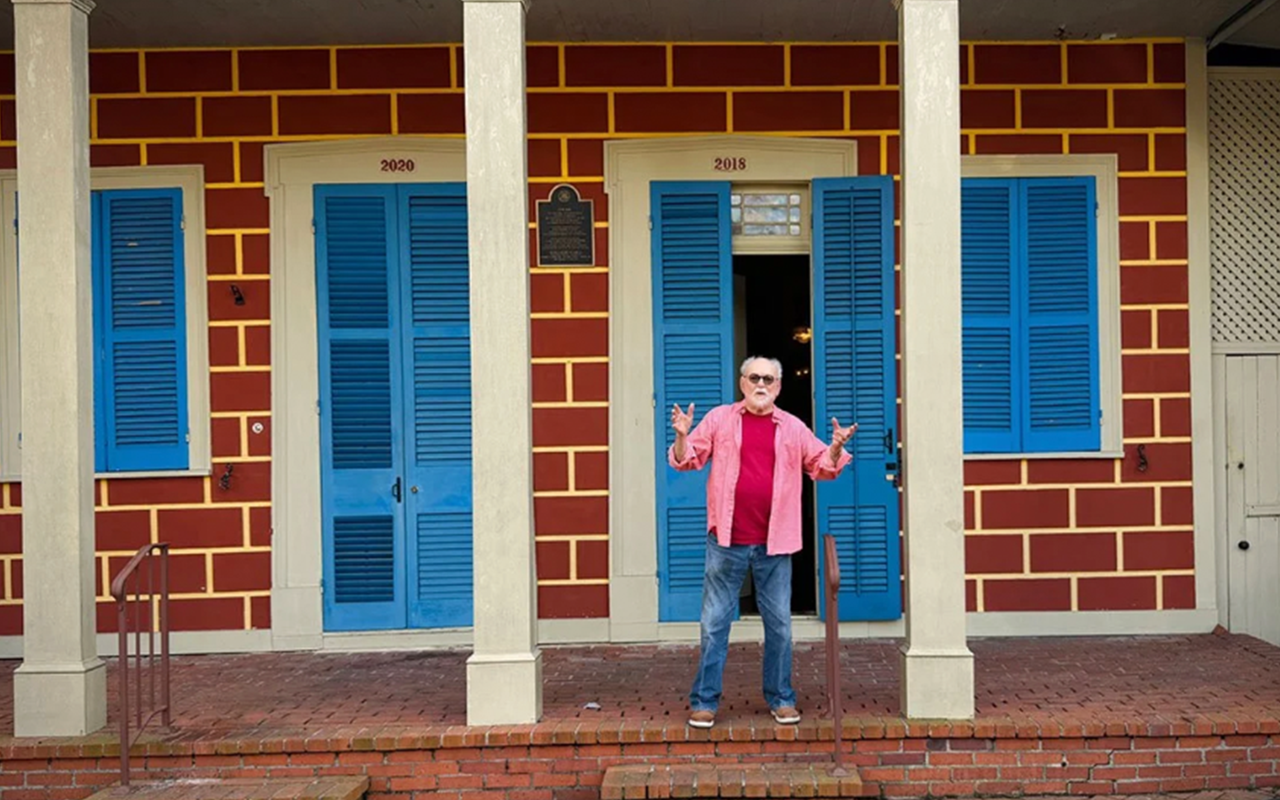 Gene Cizek on the porch of his home, Sun Oak. The house is brick with white columns and blue shutters.