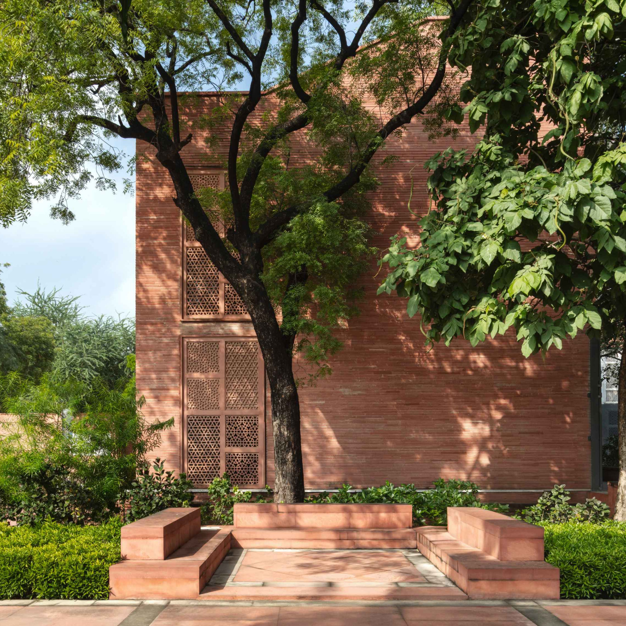 A museum facade in red brick shaded by trees.