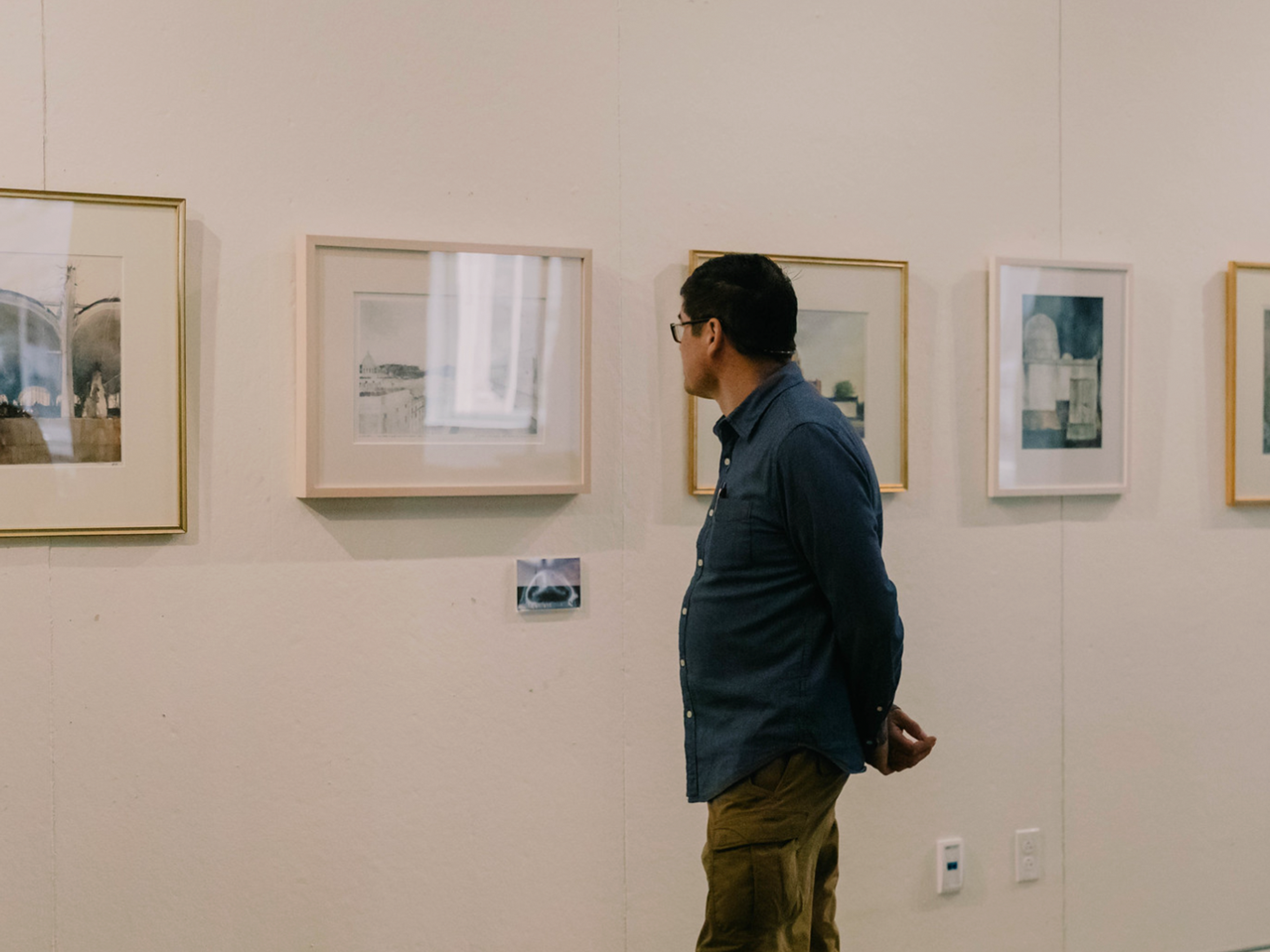 Person standing in front of and looking at paintings with hands behind his back