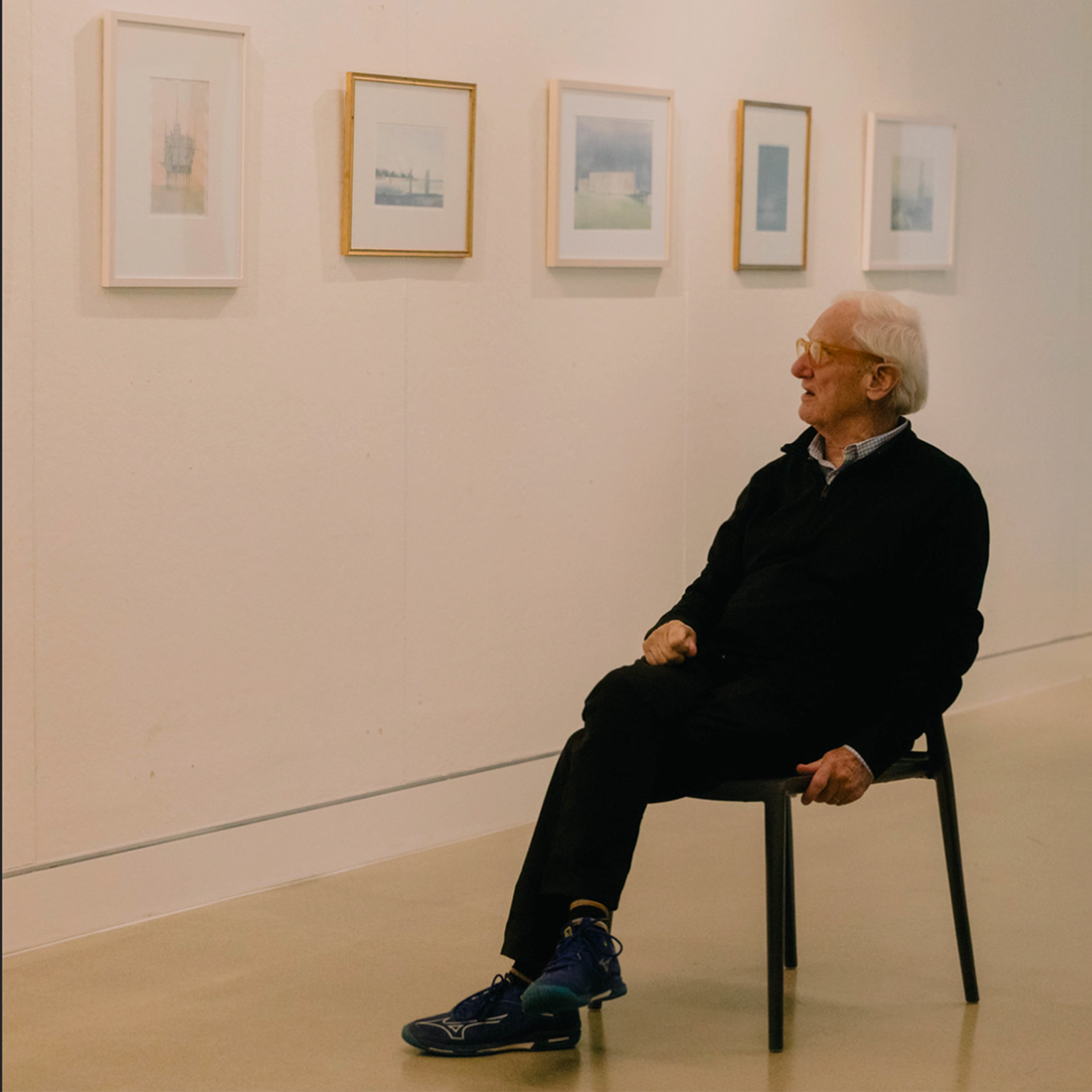 Errol Barron sitting in front of and looking at his framed work on the wall