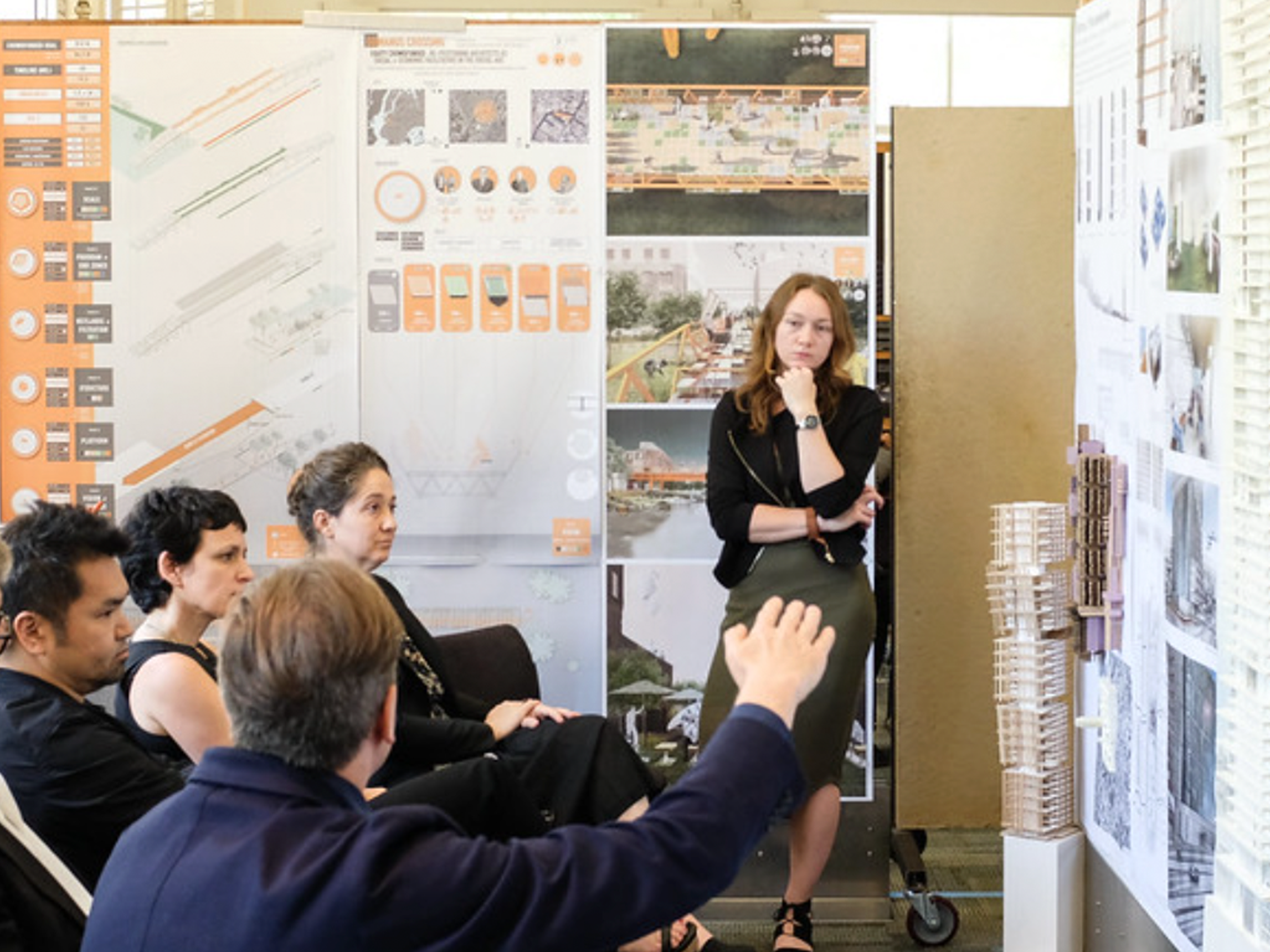 Presenter being asked a question by an audience member raising his hand, surrounded by posterboards