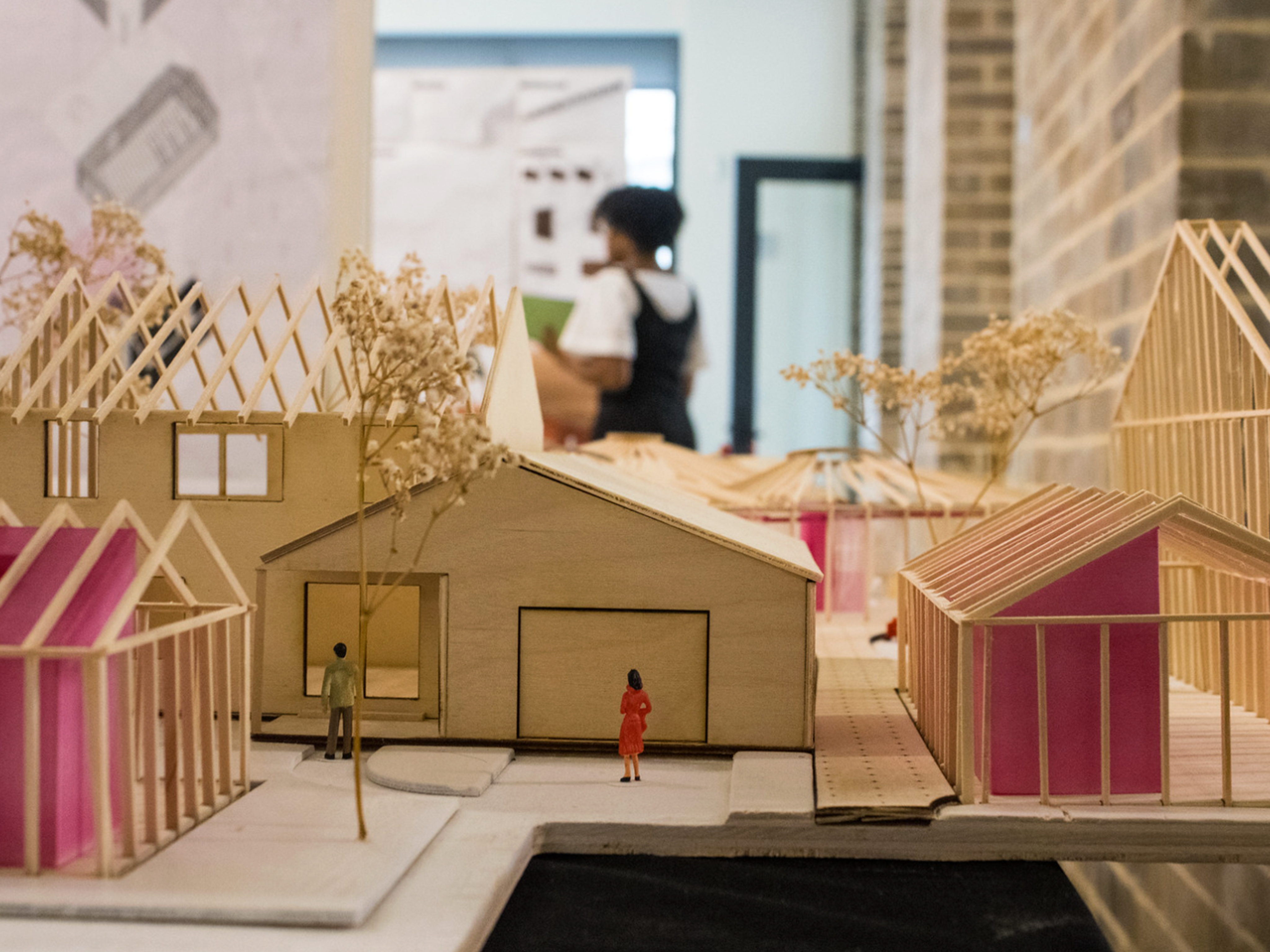 Wooden scaled models of houses with pink interiors and miniature trees and figurines outside them
