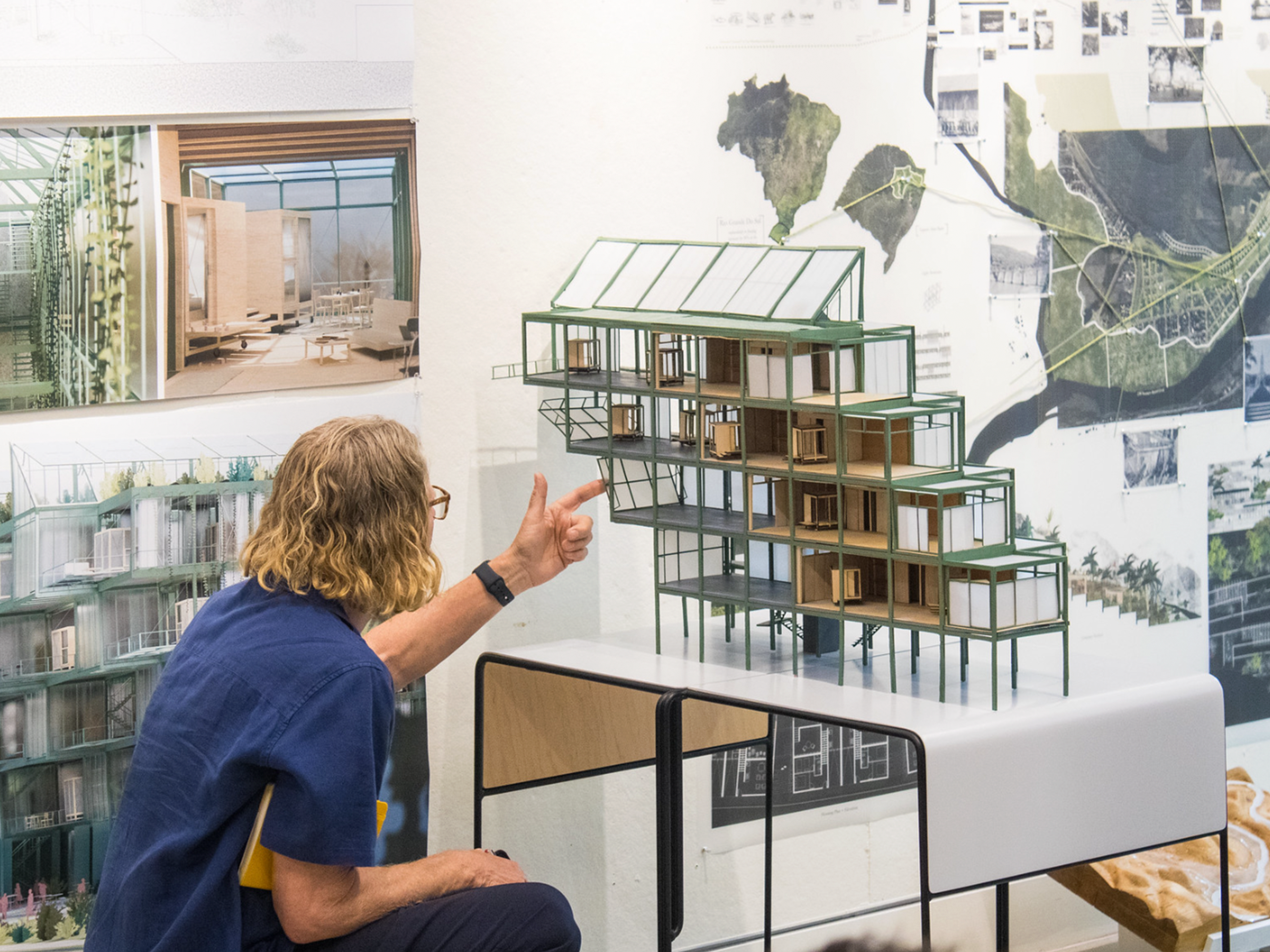 Woman in blue shirt sitting and pointing at a student's model with digital print on the wall behind it