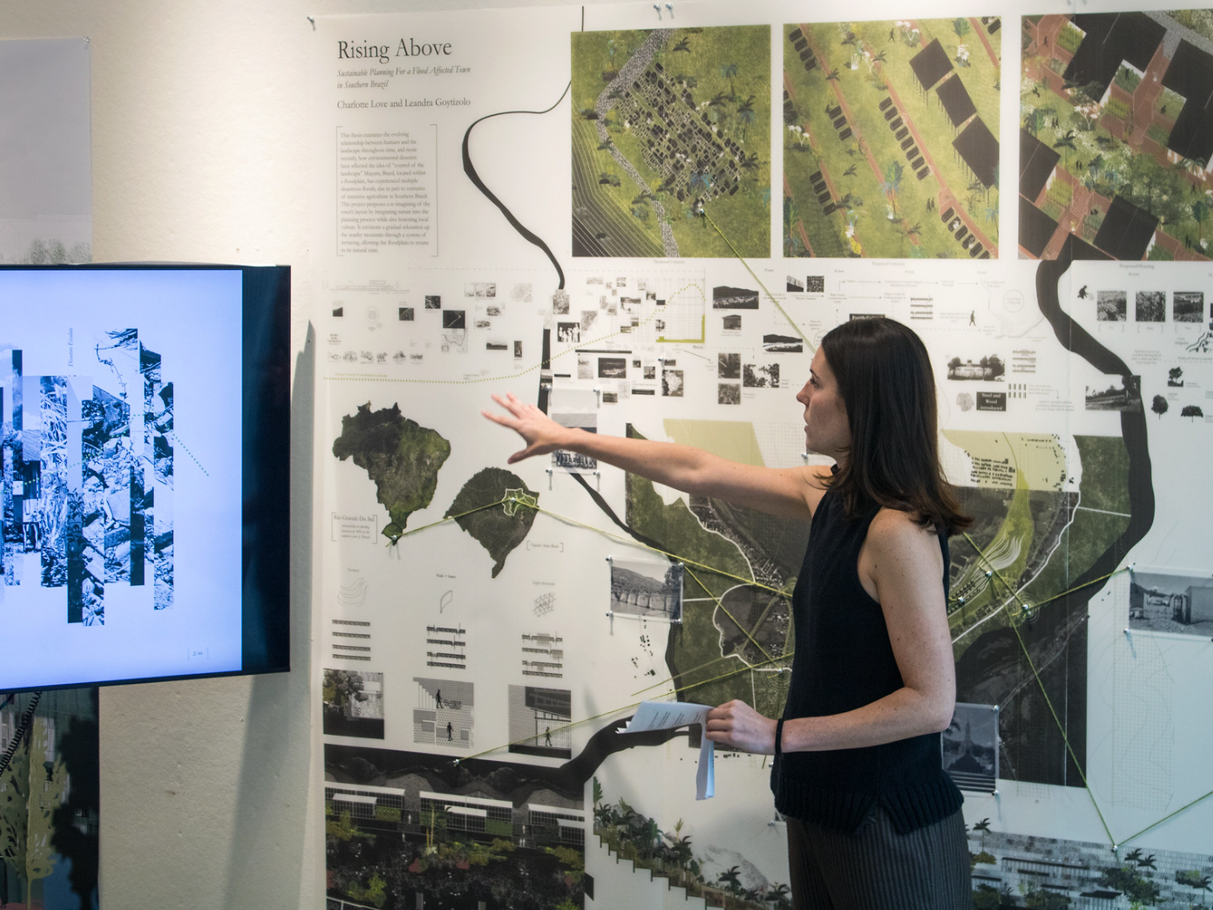 Woman in black shirt pointing at presentation on a screen, printed out images of work behind her