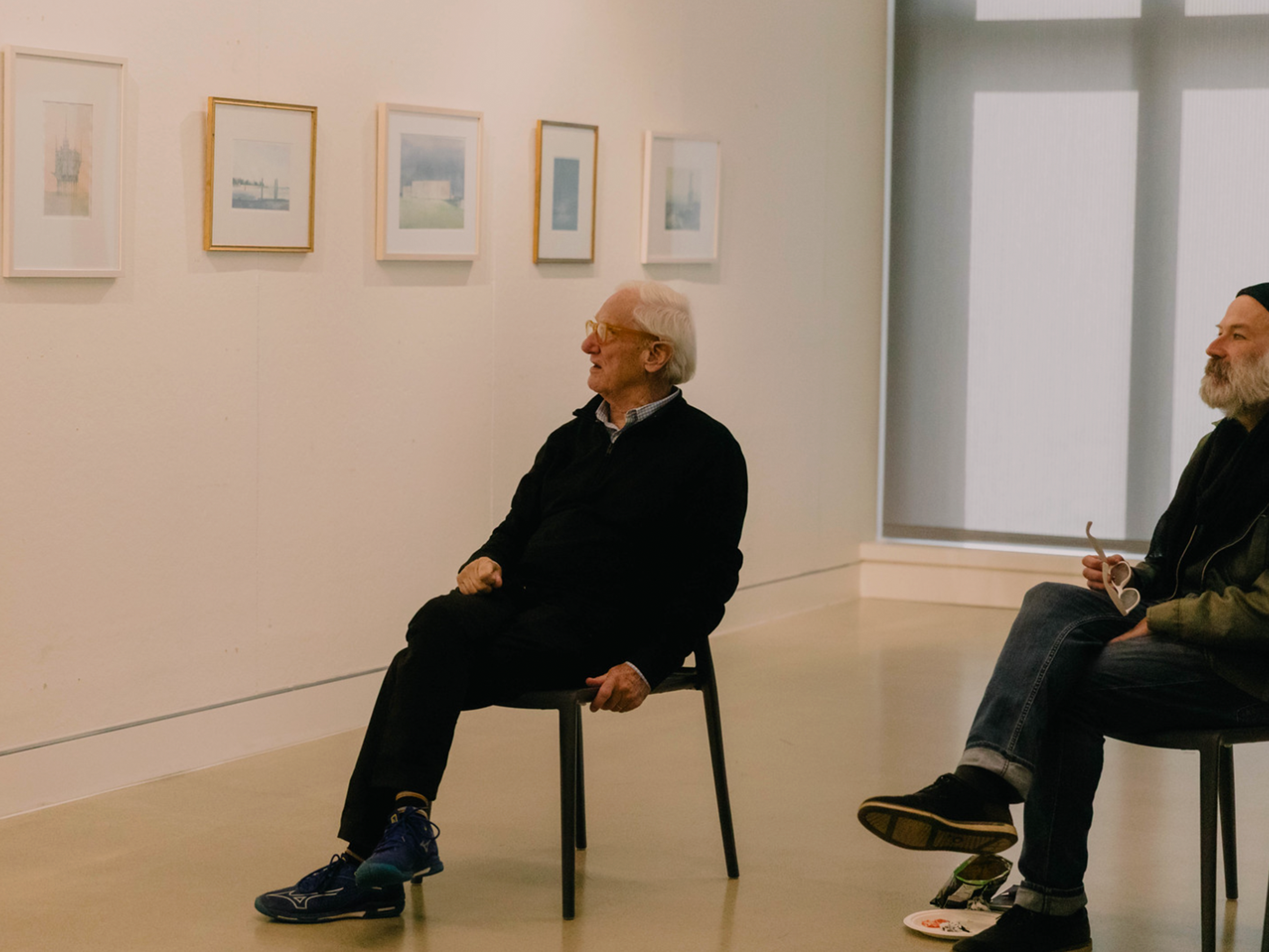Errol Baron and another sitting in front of framed paintings