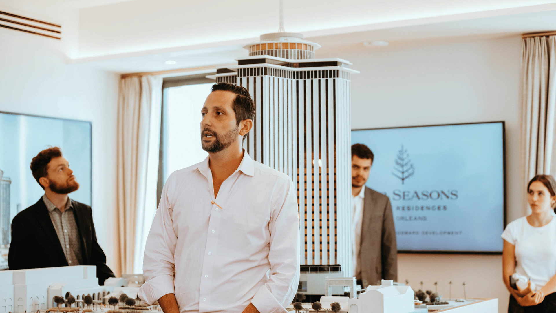 Photo of someone speaking in front of a group in an open room with a large hotel model in the background.