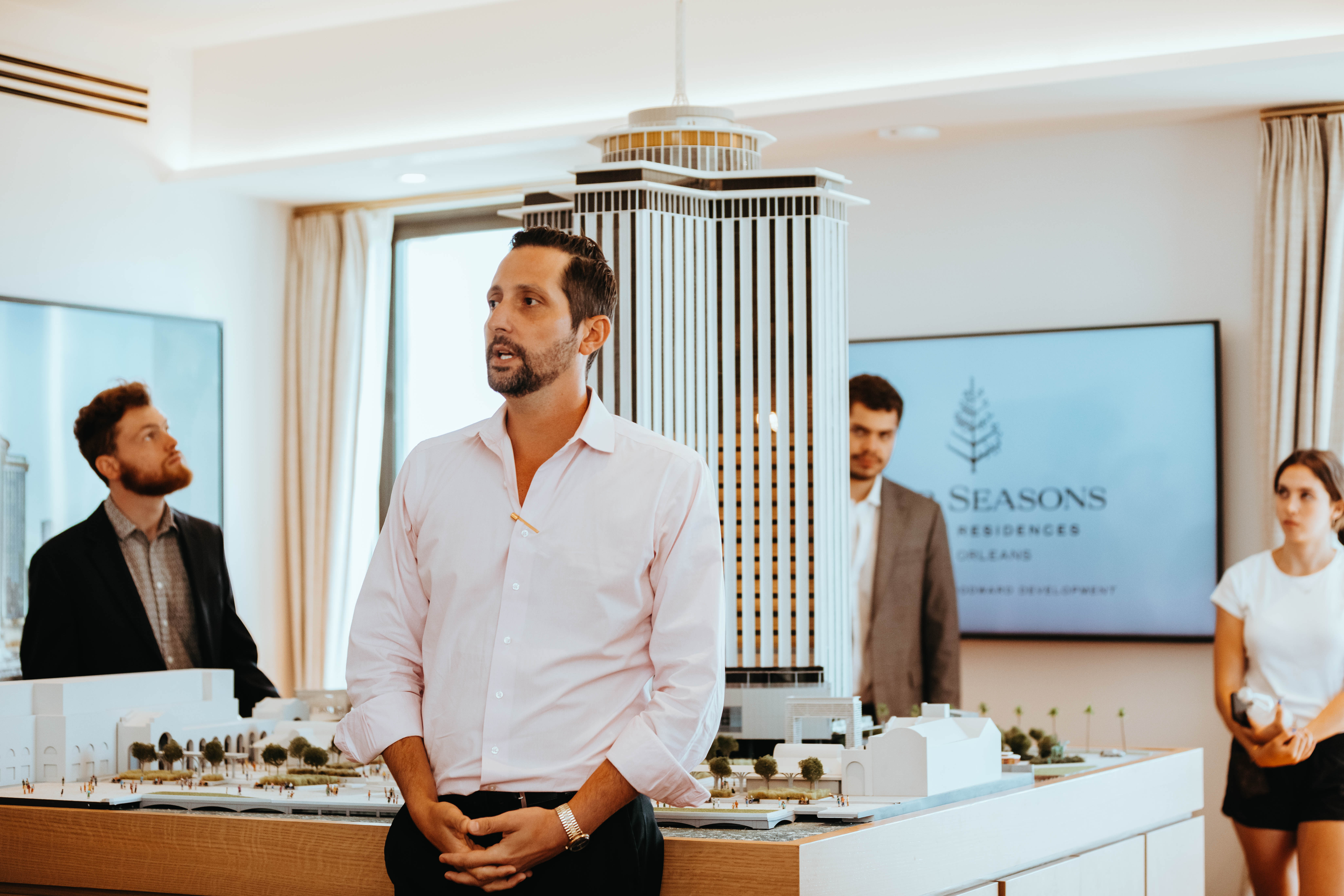 Photo of someone speaking in front of a group in an open room with a large hotel model in the background.