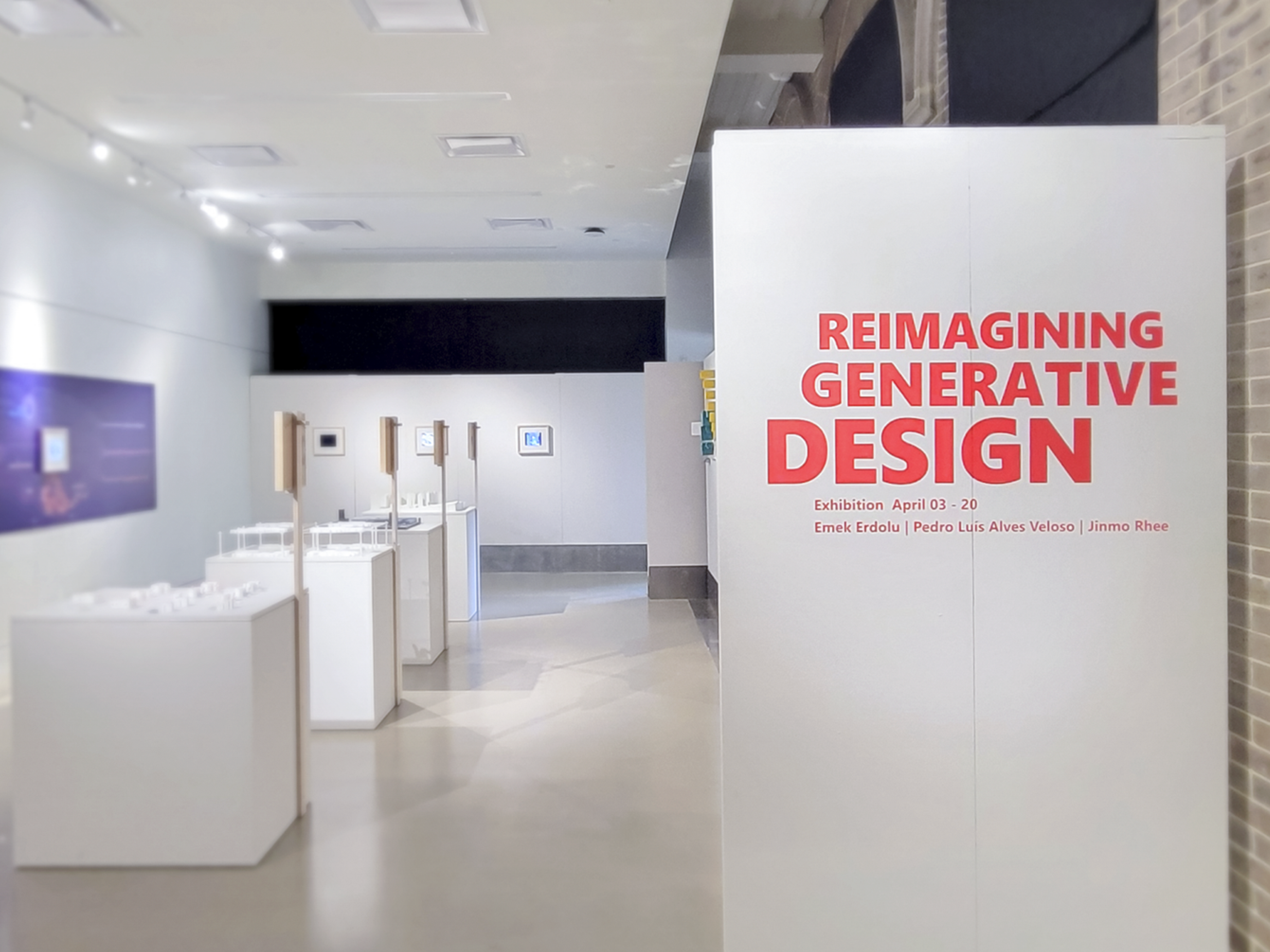 Entrance to the exhibit with a white column on the right side saying "Reimagining Generative Design" in red text with the curators' names below.