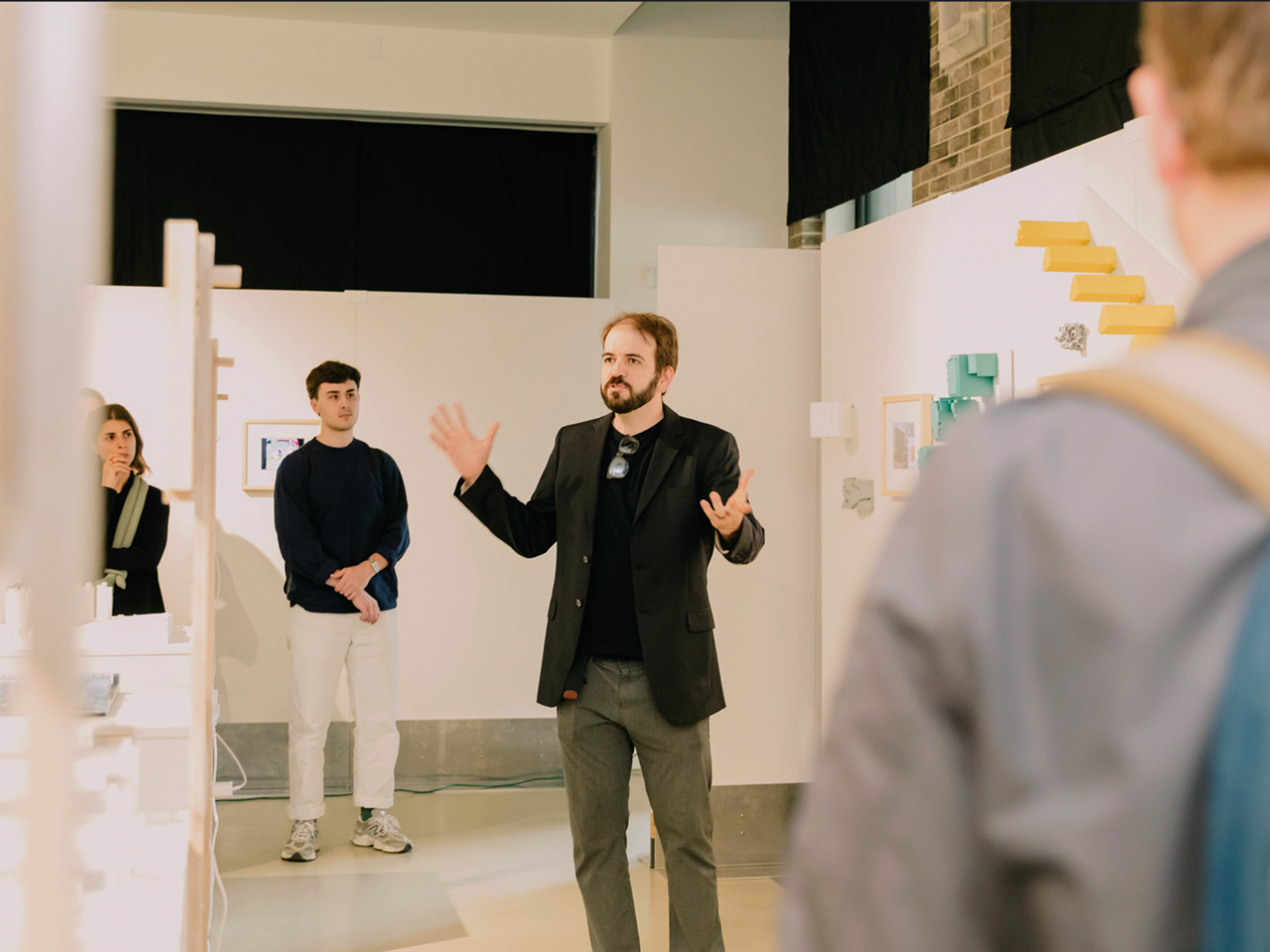 Pedro Veloso in a black suit jacket with green pants presenting the exhibit to students