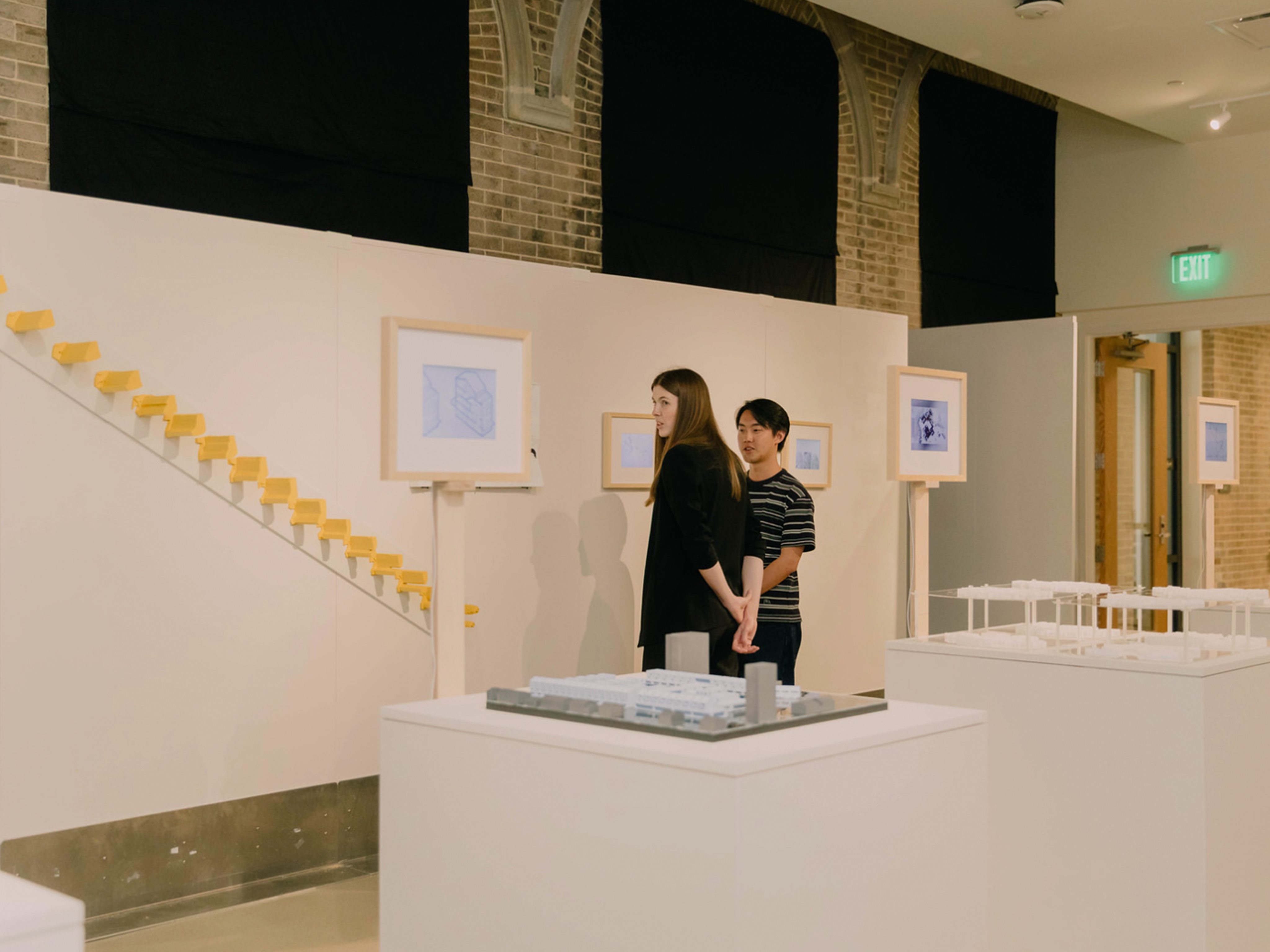 Two students looking at the exhibit with models in the middle of the room in front of them and the display wall
