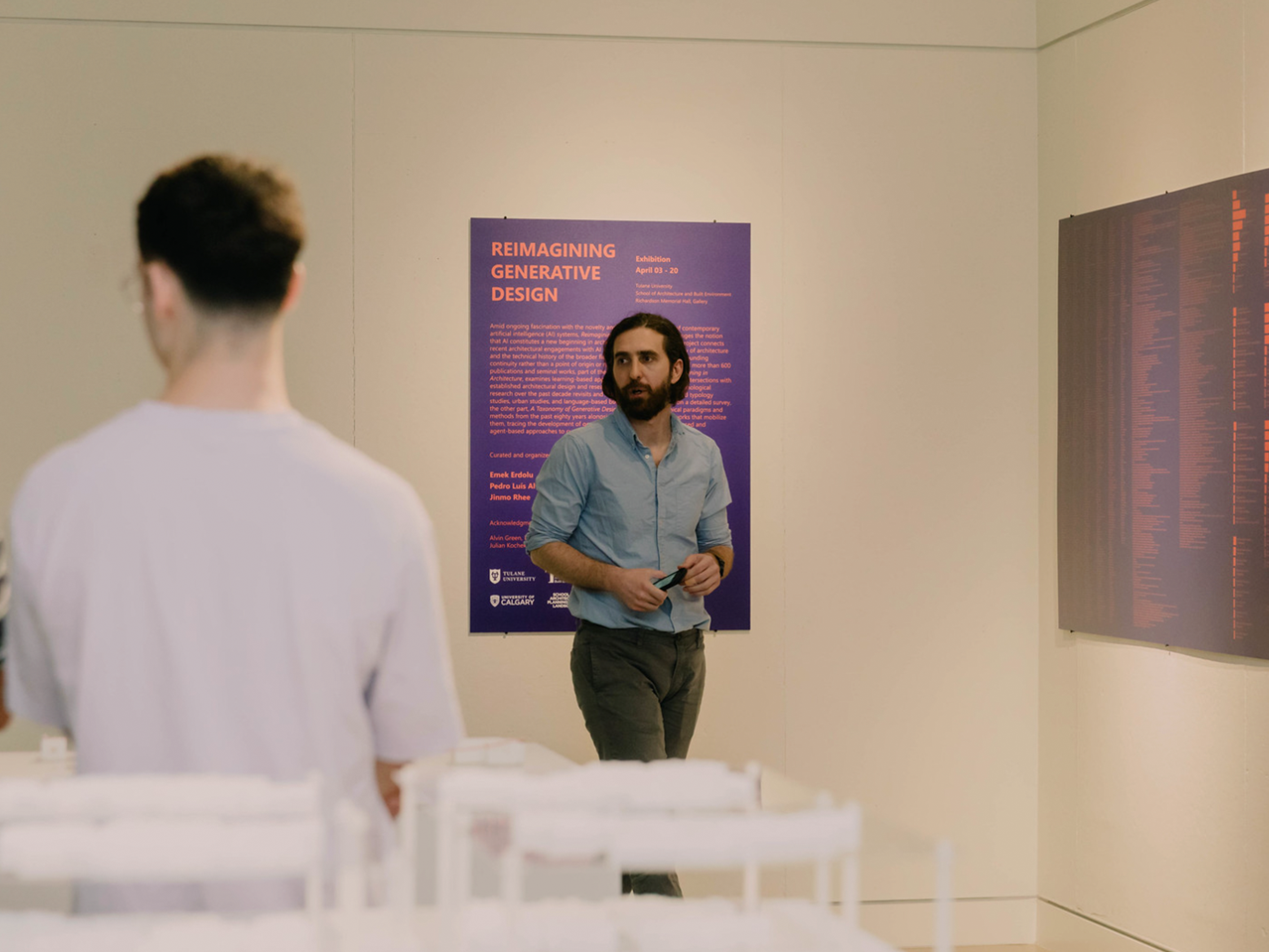 Emek Erdolu standing in front of purple exhibition title poster