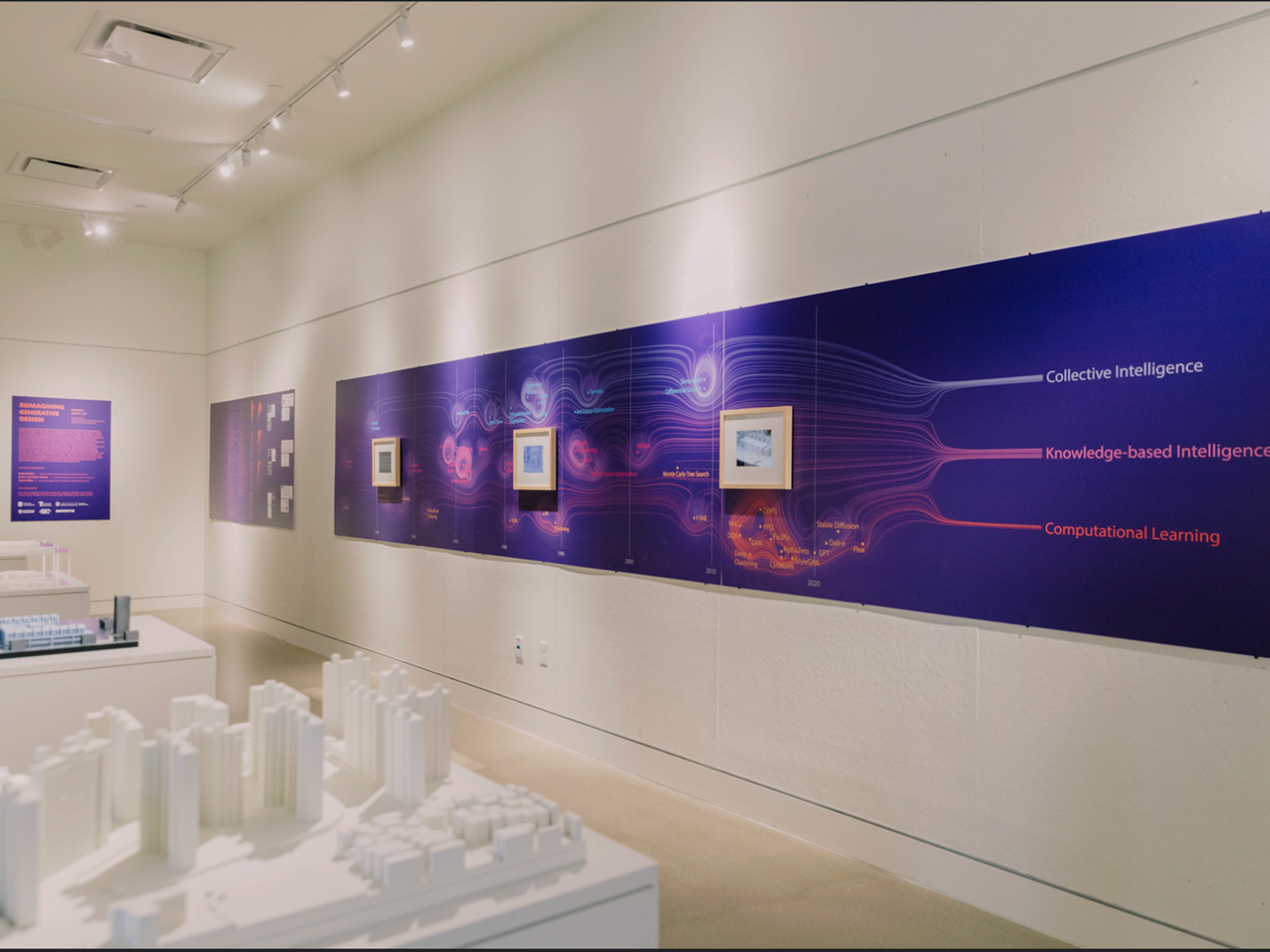 Small building models on tables in the middle of the room with purple display posters on the walls