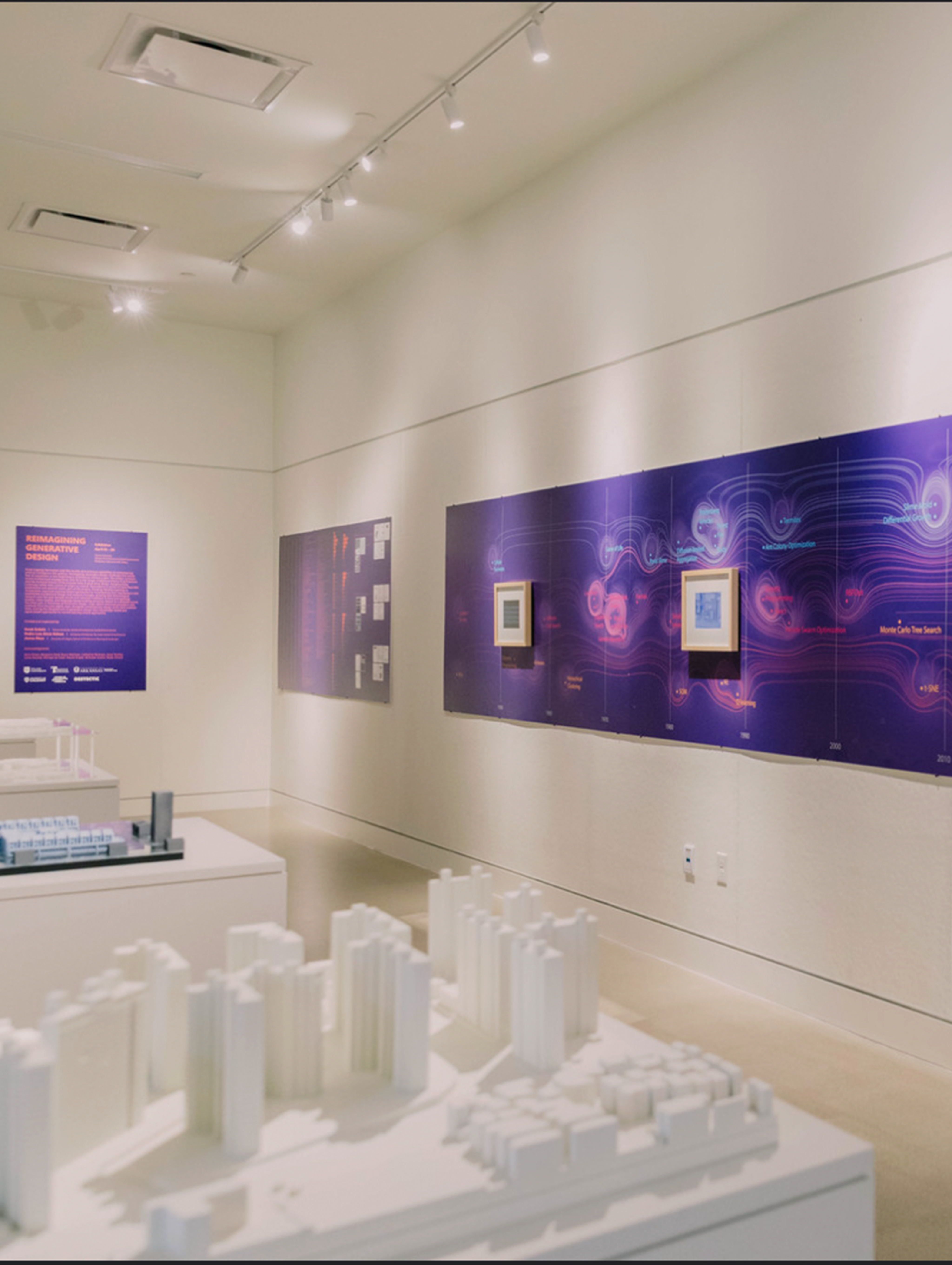 Small building models on tables in the middle of the room with purple display posters on the walls.