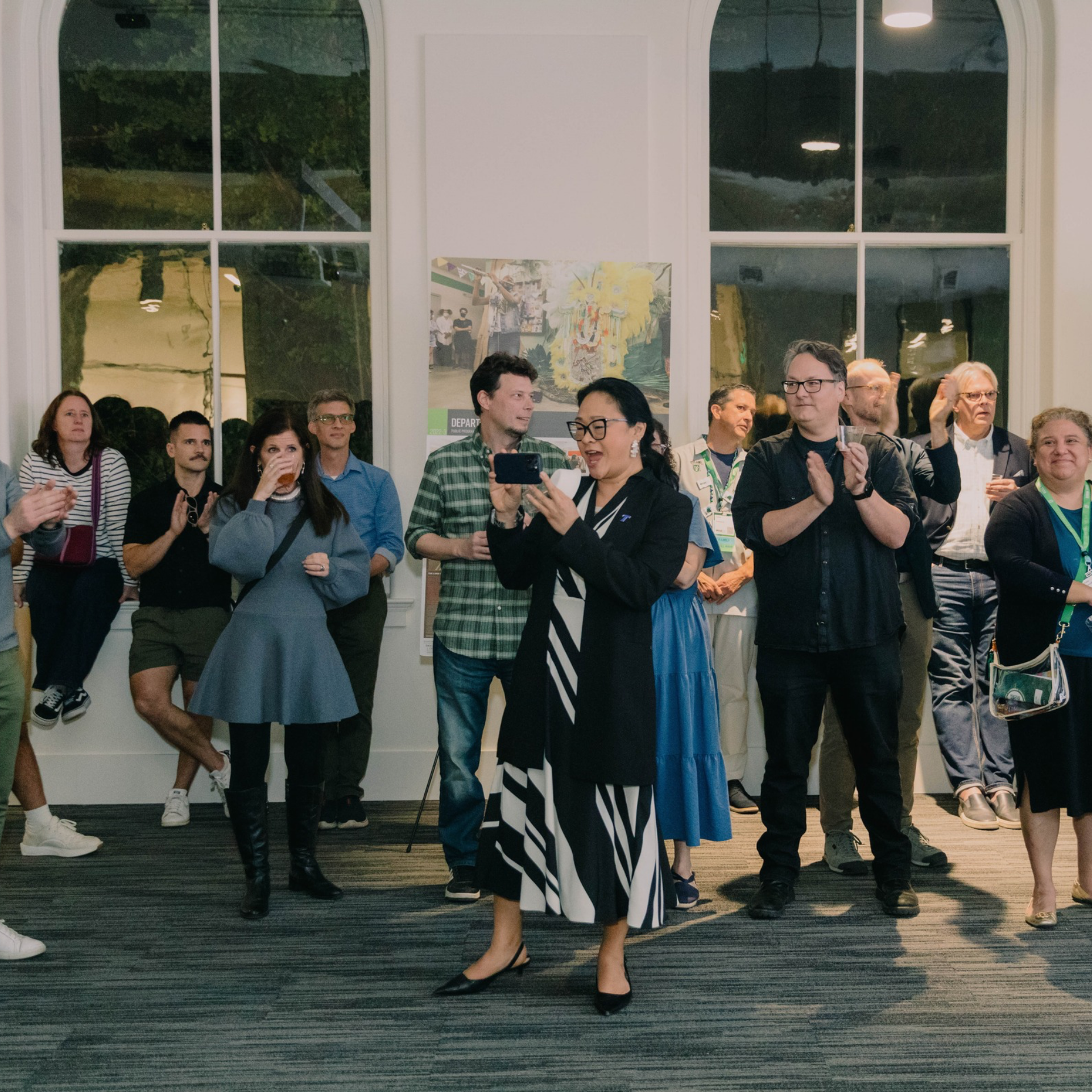 A crowd stands and claps during a reception style event inside a large room.