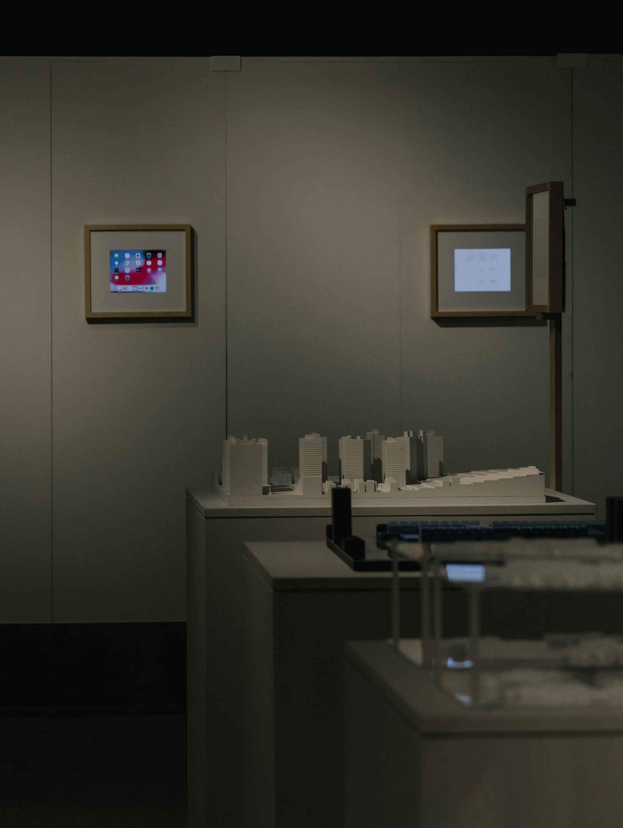 Small building models on tables in the middle of an empty, dark gallery space.
