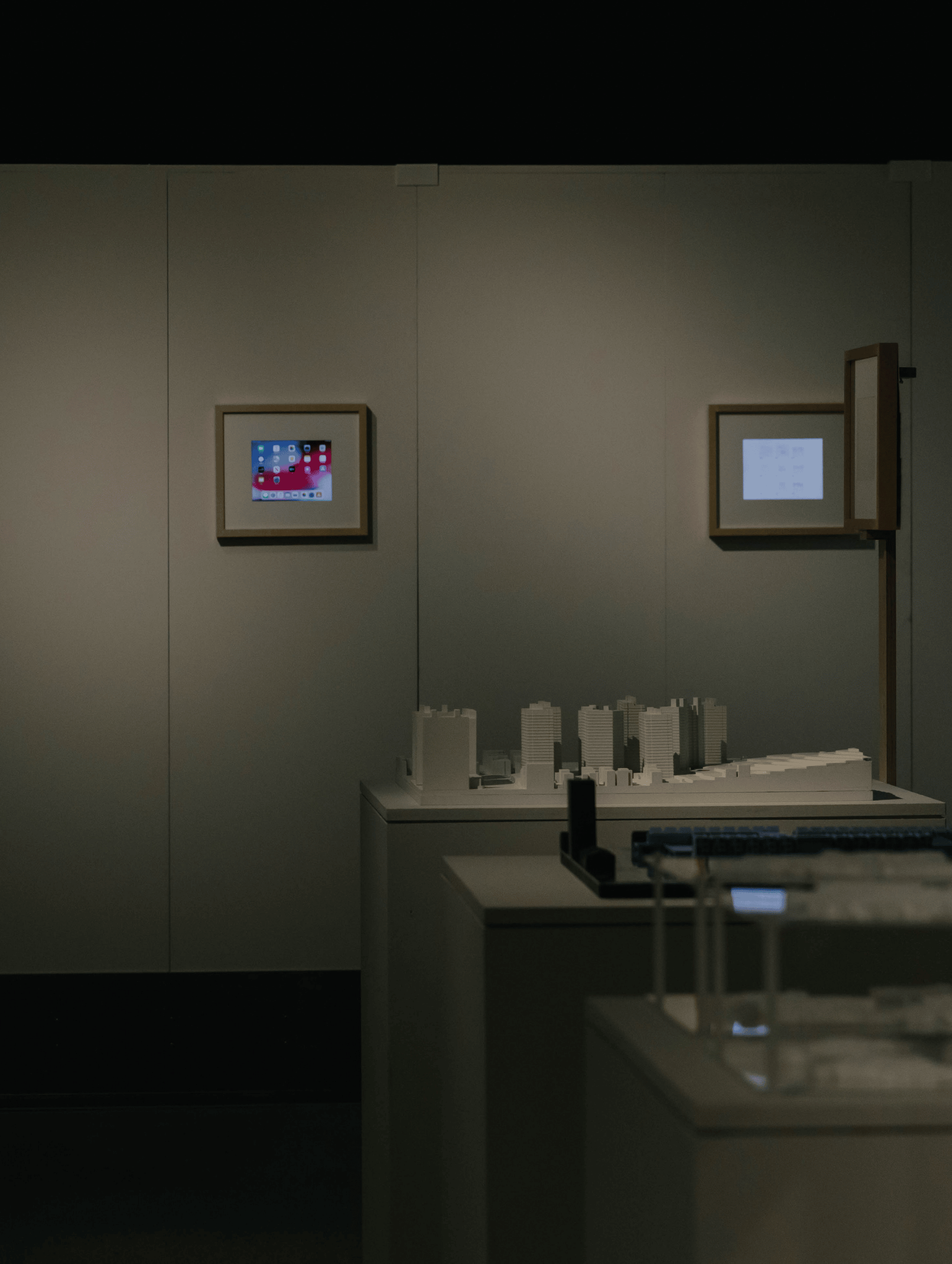 Small building models on tables in the middle of an empty, dark gallery space.