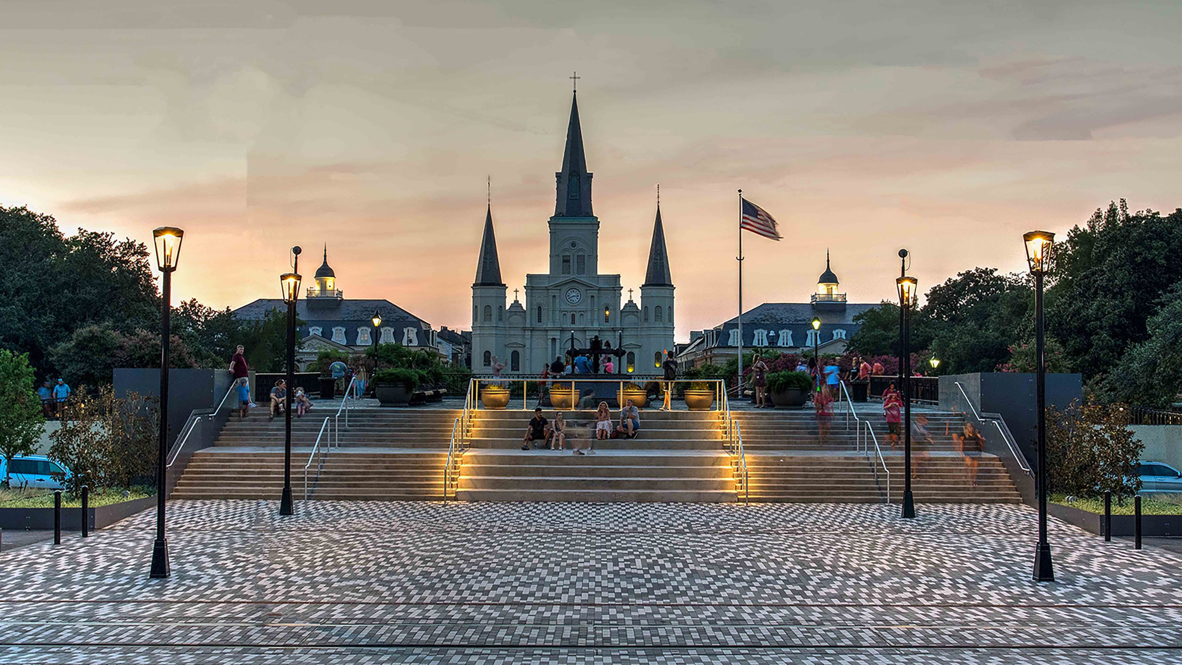 Outdoor plaza at dusk with wide ascending stairs in the background and St. Louis Cathedral in the distant background