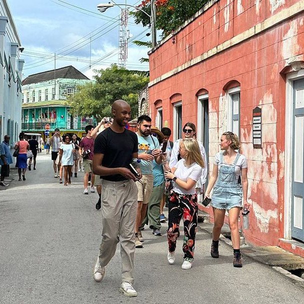 Large group of students from US, UK, Caribbean walk down a narrow Caribbean street with historic buildings on either side of them and in the background