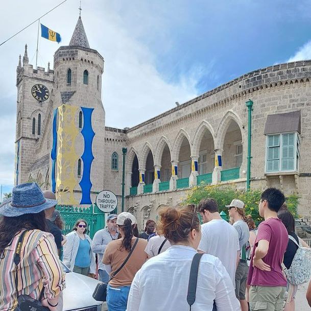 View from behind the backs of a group of diverse students looking at a large stone medieval cathedral with a clock tower and turret.