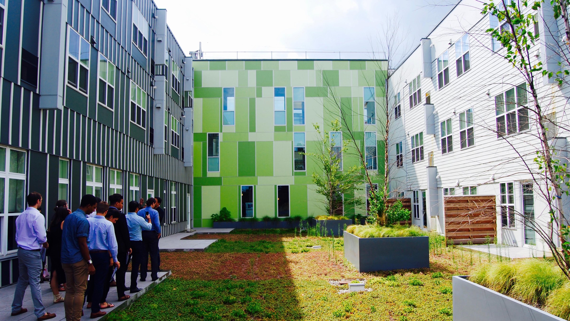 Group of suit-wearing students walk toward the back wall of a square courtyard inside a modern design building 