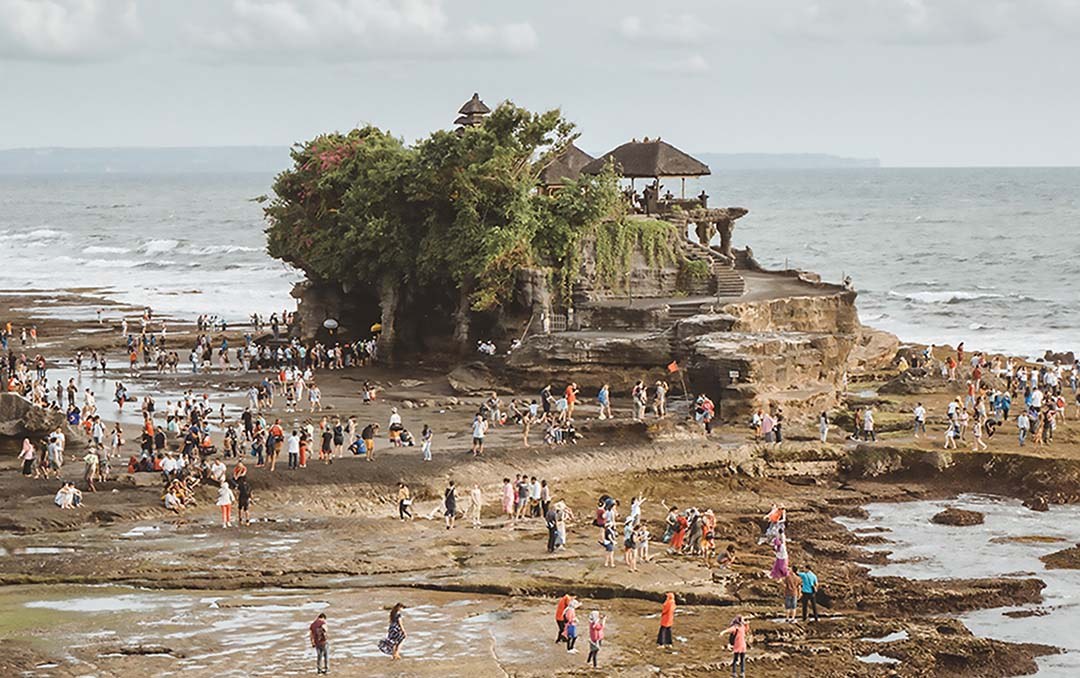 Aerial photo of a rocky beach with dozens of people walking on the beach and a small cliff in the background