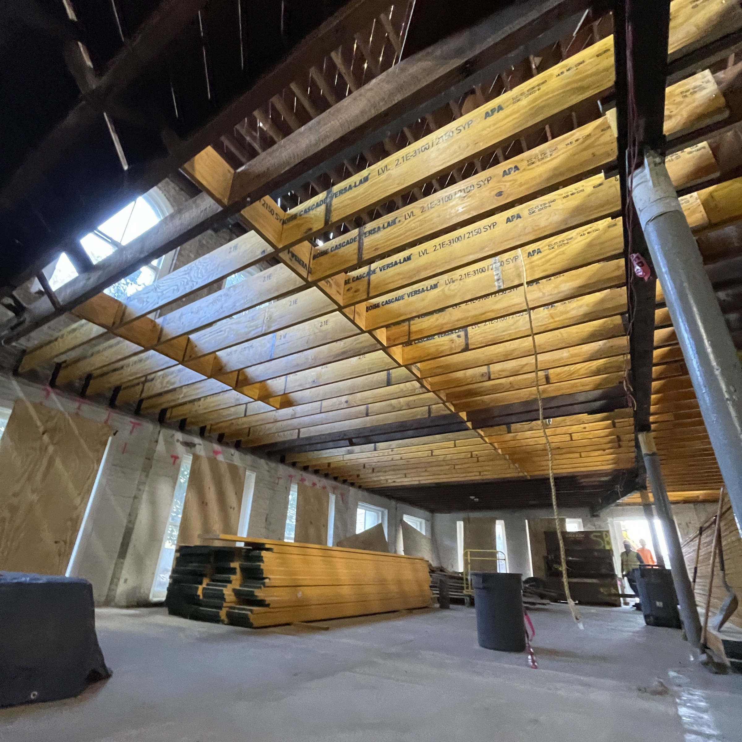 Interior photo of a lower level of renovation project, looking up from a concrete floor through new floor beams above