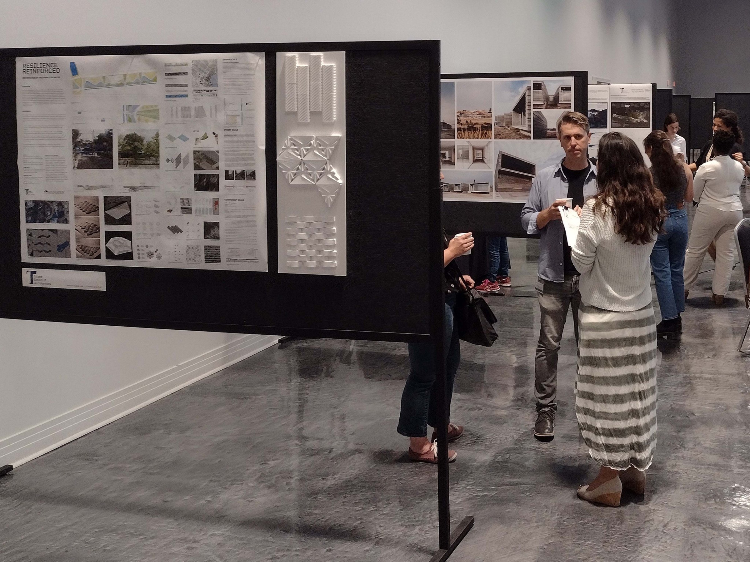 People stand talking and looking at large posters pinned to temporary display boards inside a large conference room floor