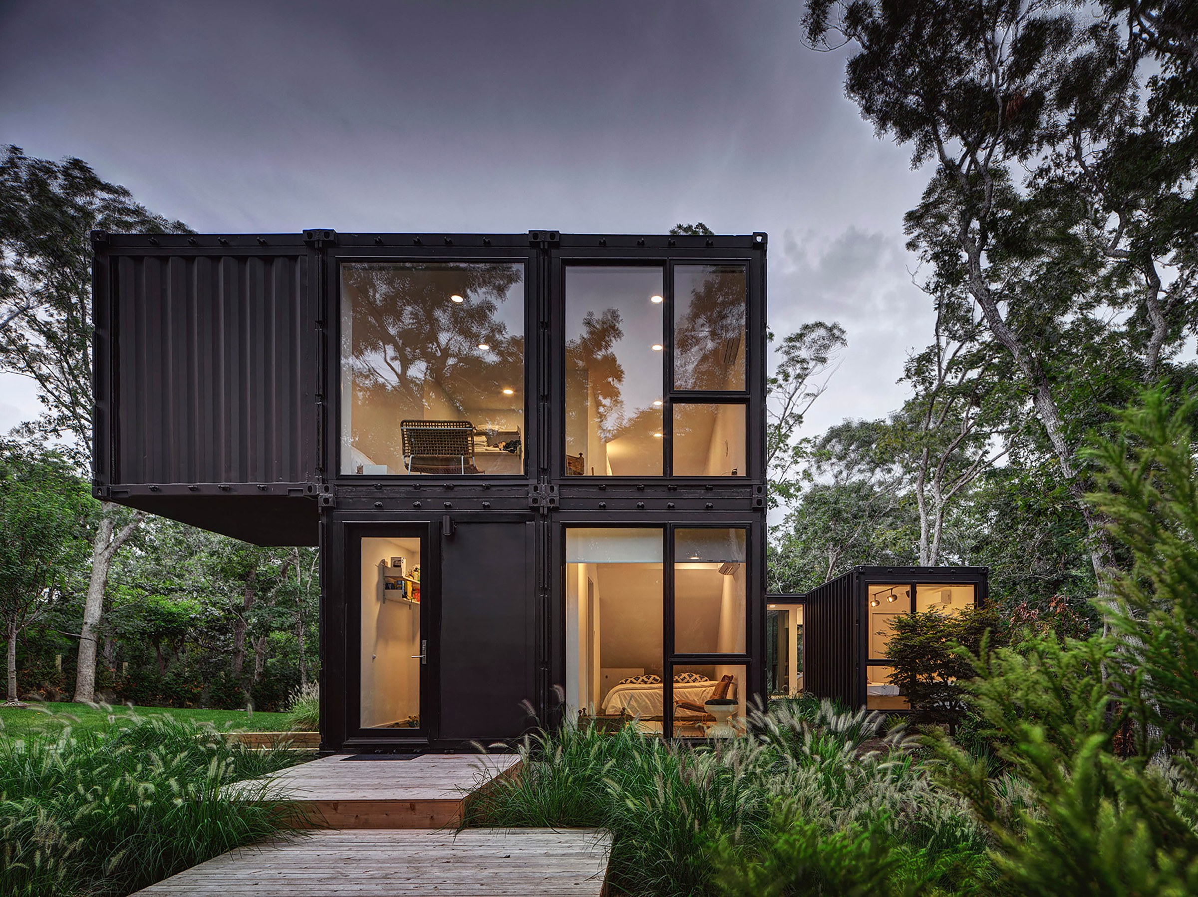 Black modern modular house with large windows and lush green trees surrounding