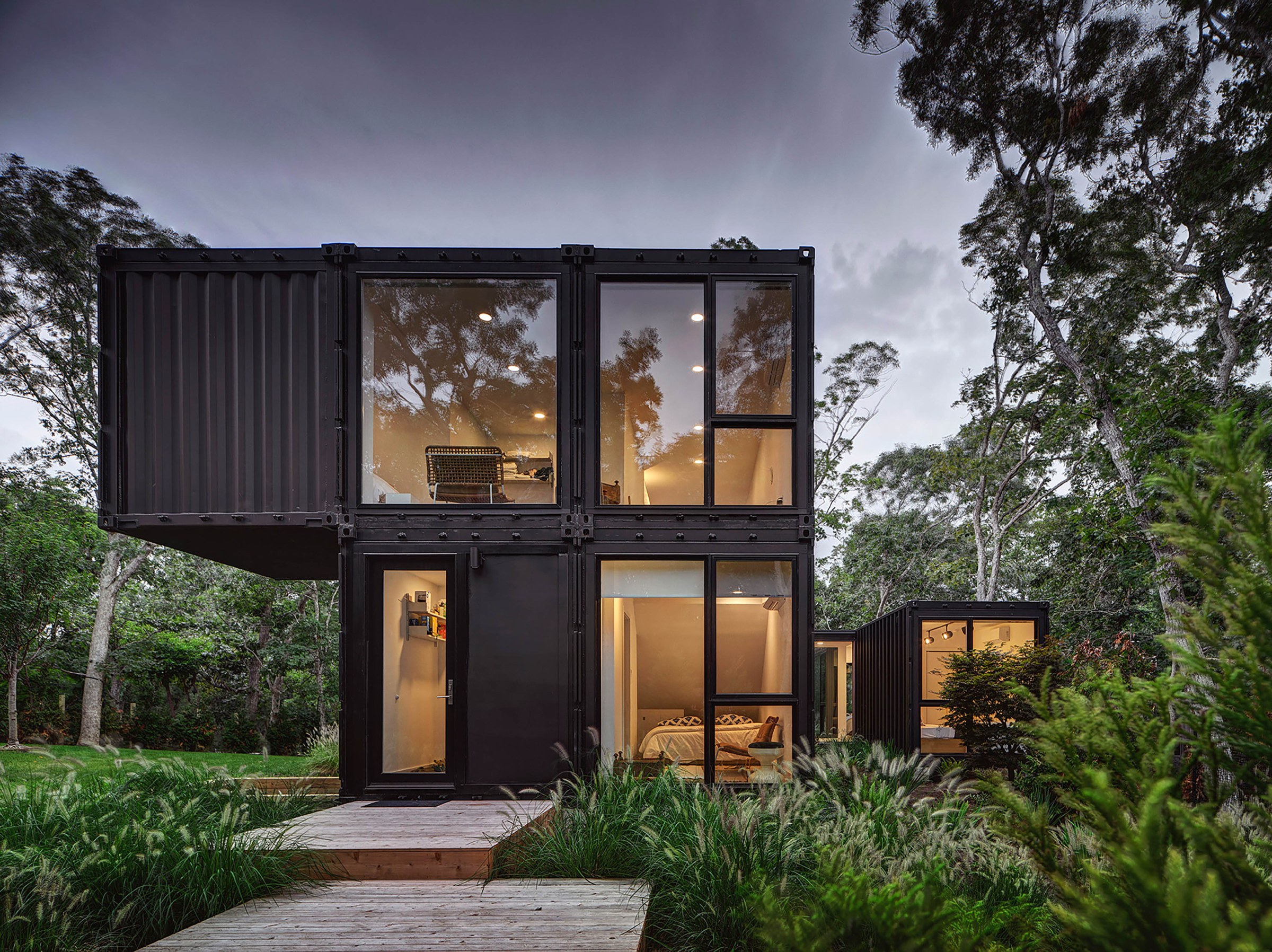 Black modern modular house with large windows and lush green trees surrounding 