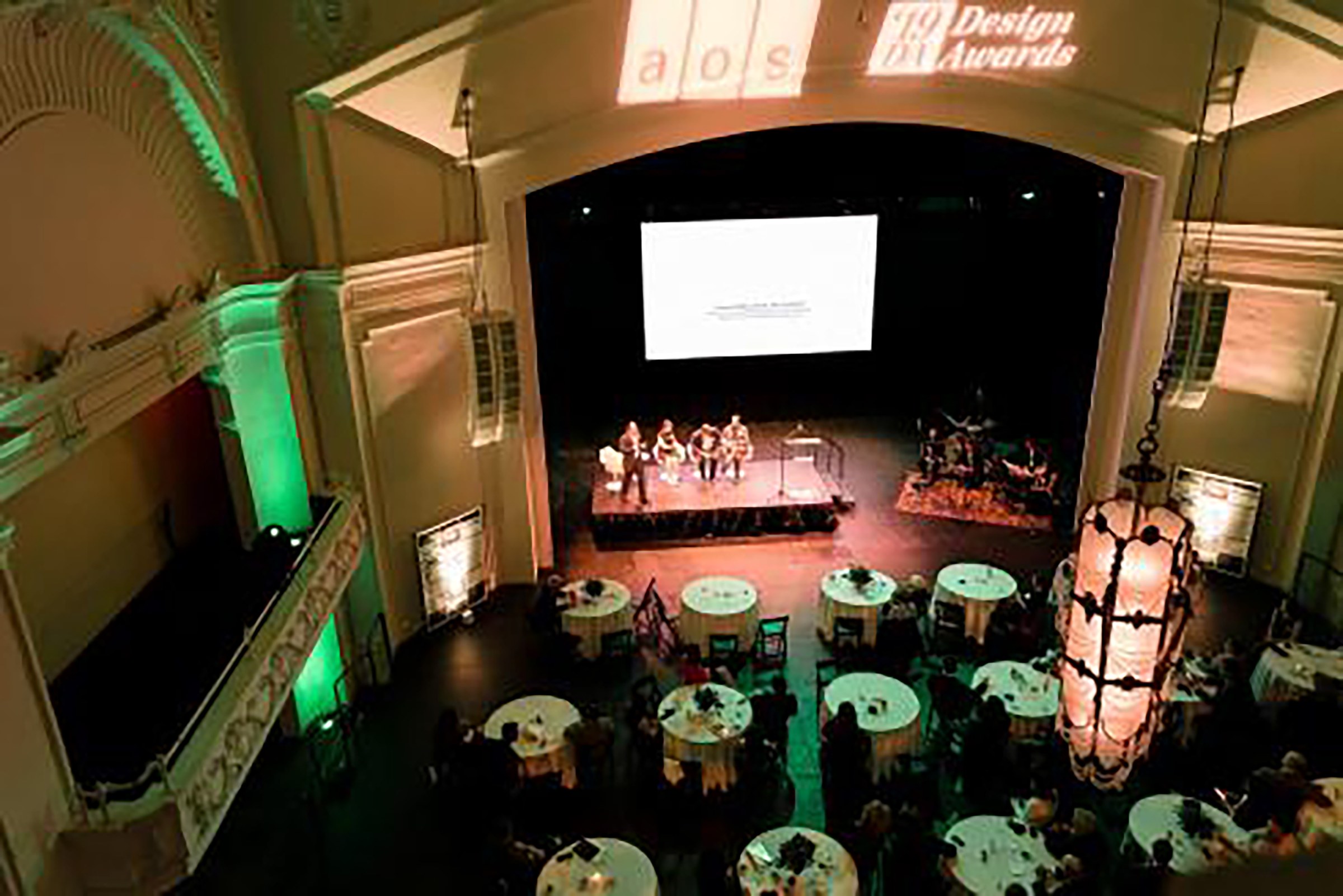 Aerial shot of awards ceremony with white table cloth covered tables and presenters on stage