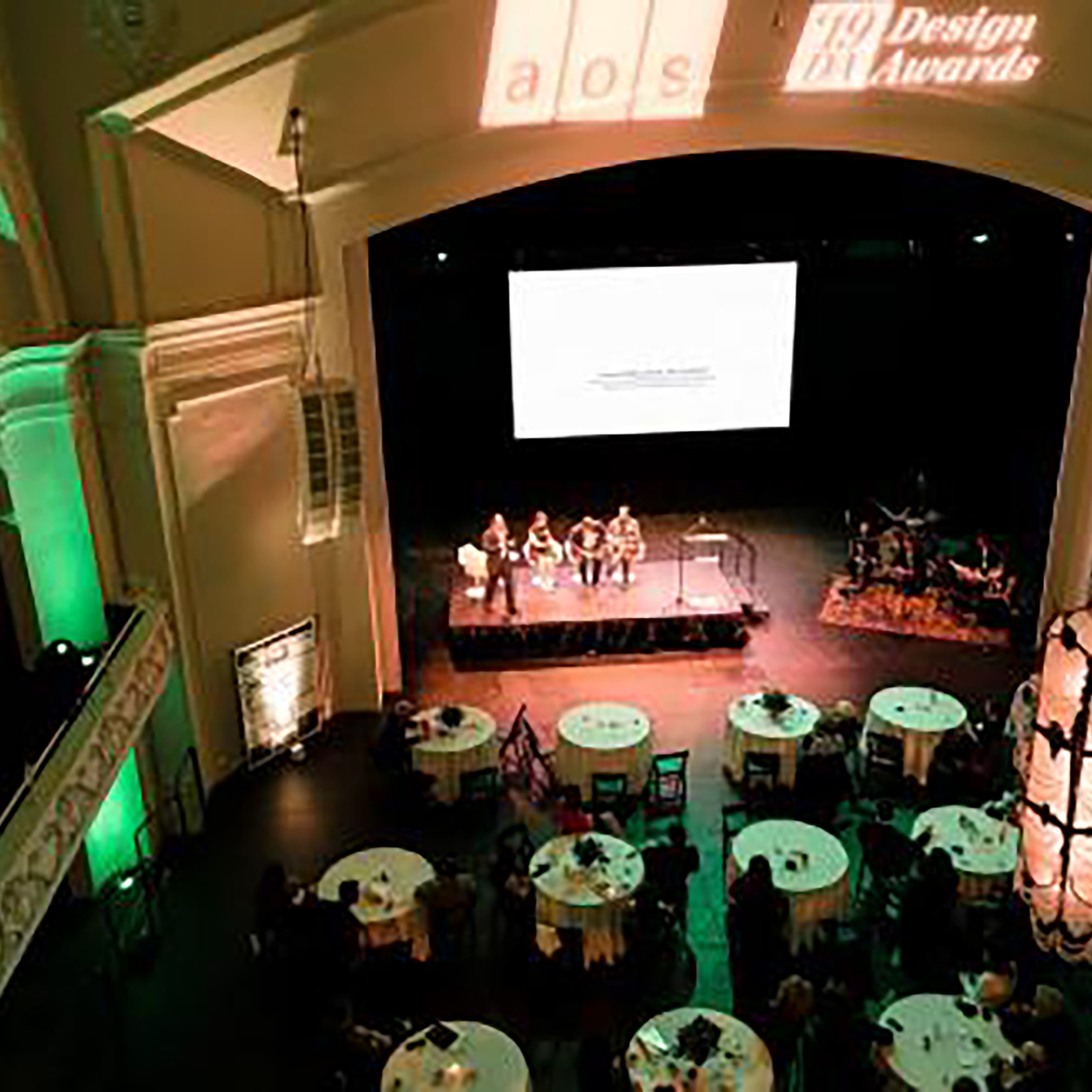 Aerial shot of awards ceremony with white table cloth covered tables and presenters on stage