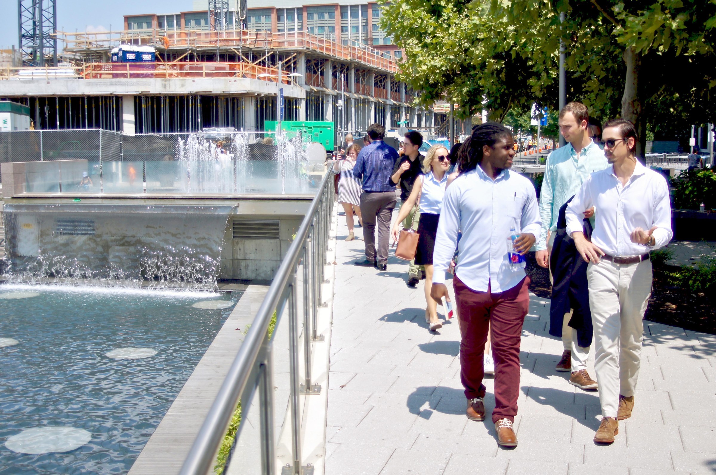 Group of people walking alongside a water feature with construction in the background