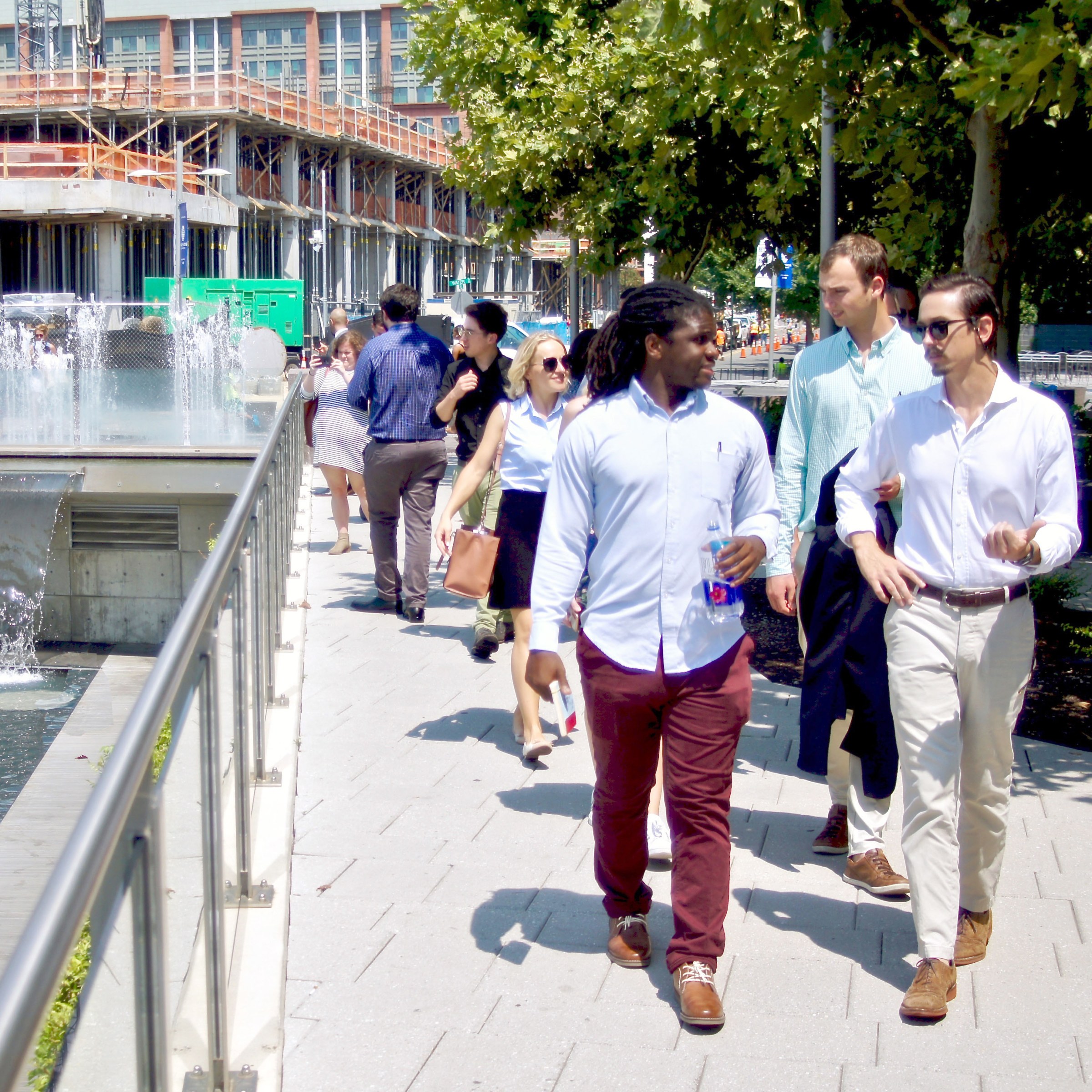 Group of people walking alongside a water feature with construction in the background