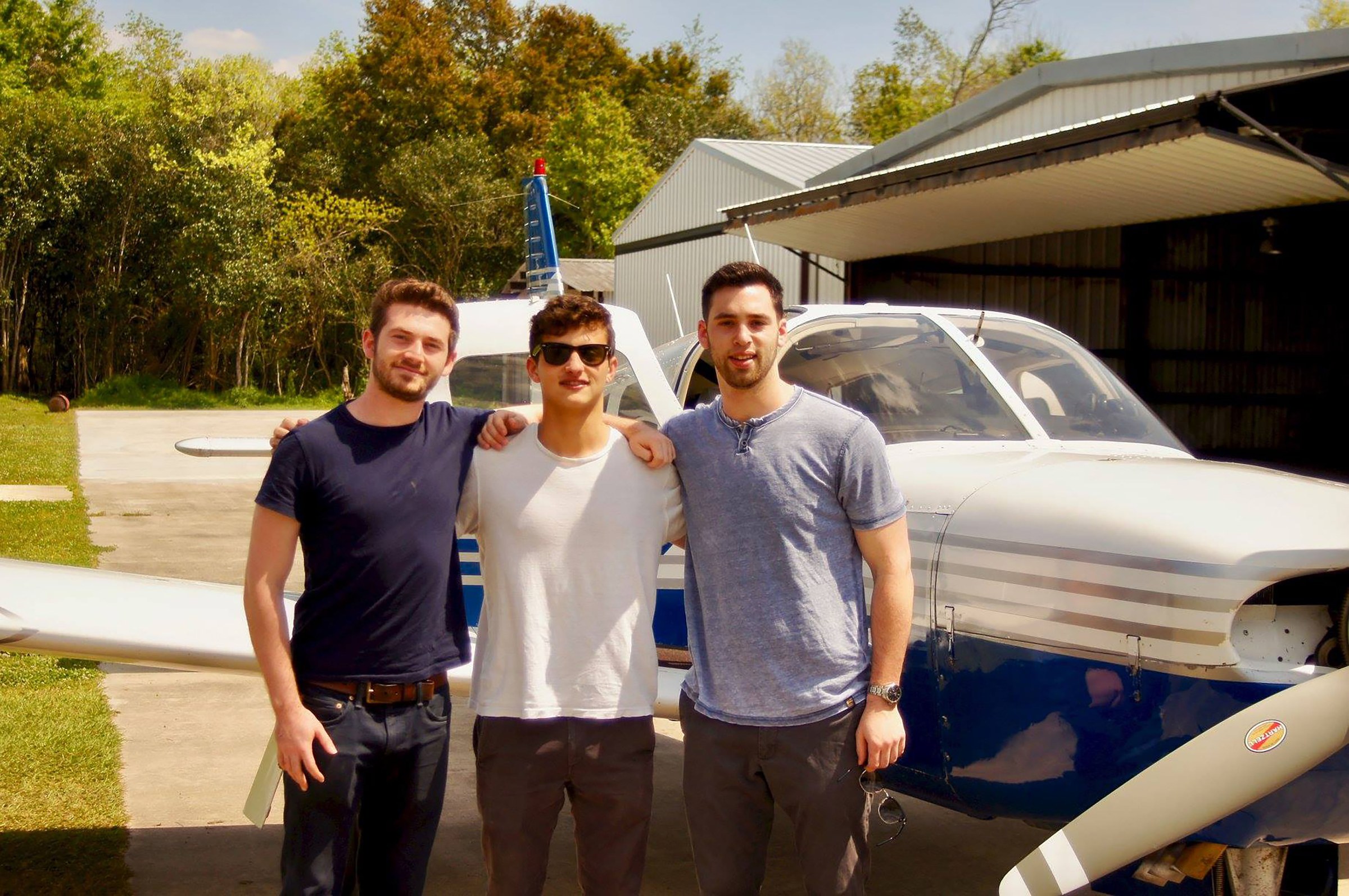 Photo of three students in front of a small propeller plane