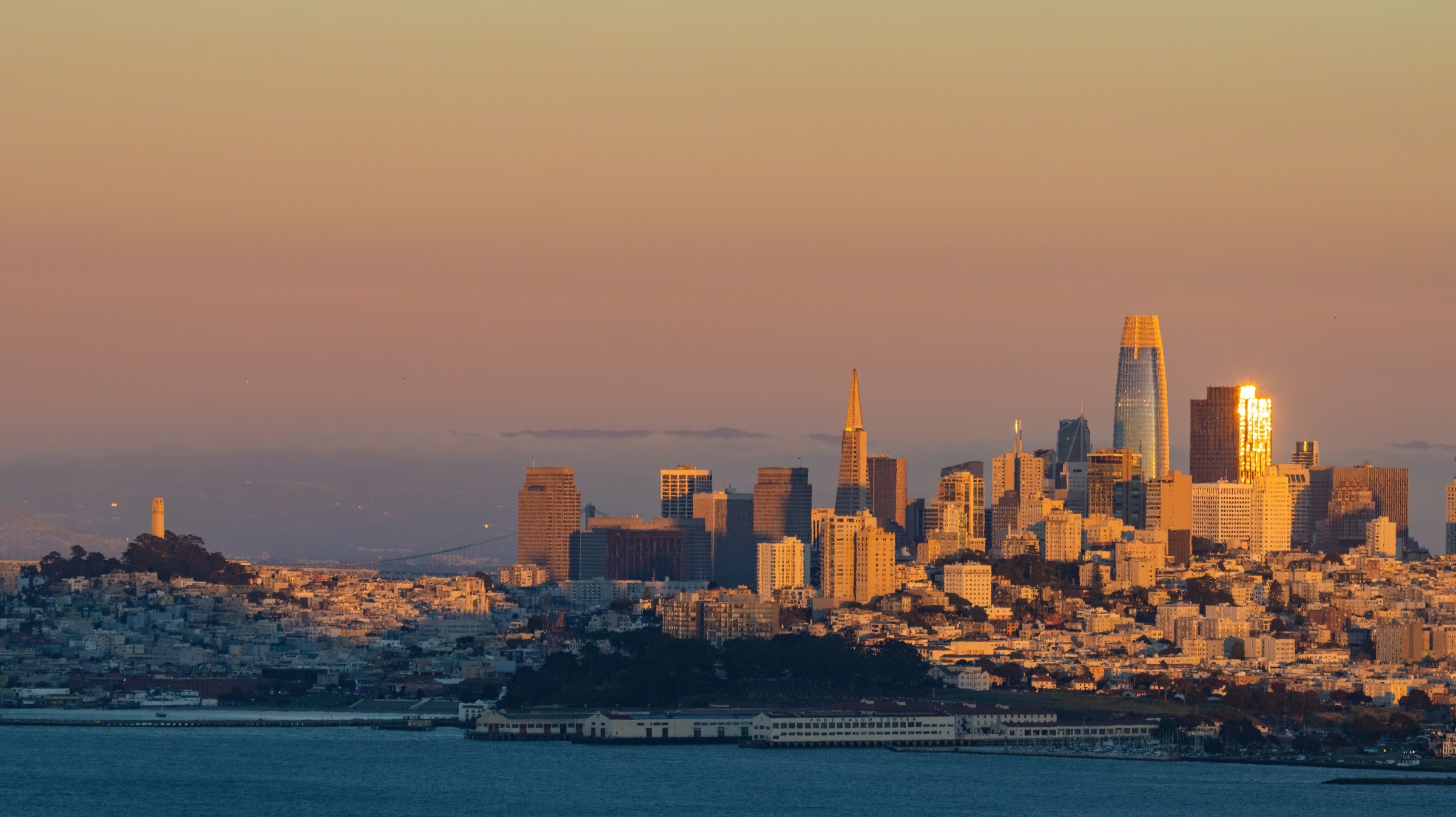 Skyline of San Francisco at sunset with downtown's tall buildings in the distance and the bay in the foreground
