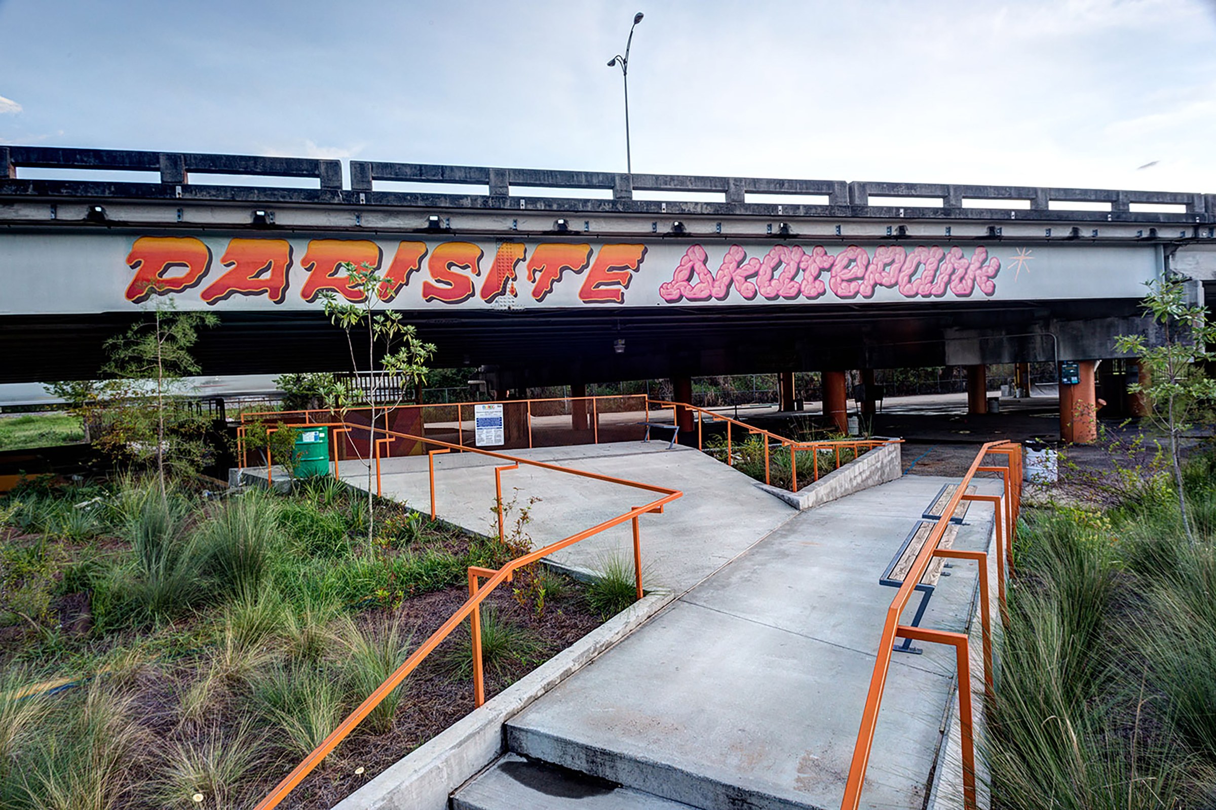 Photo of Parasite Skatepark with orange railings and greenery