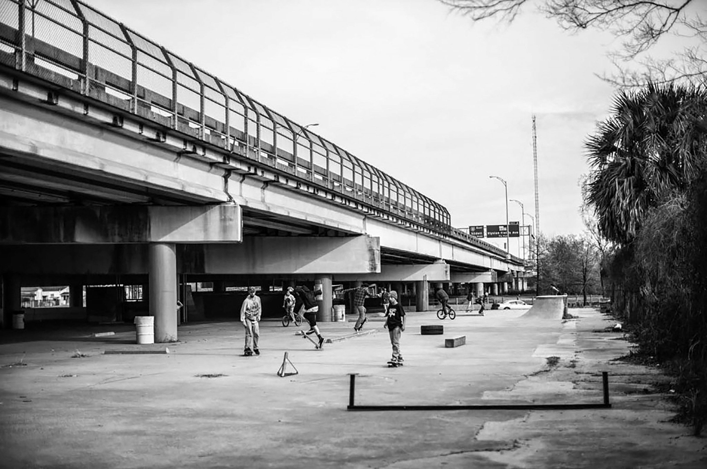 Black and white photo of group of people skateboarding under an overpass