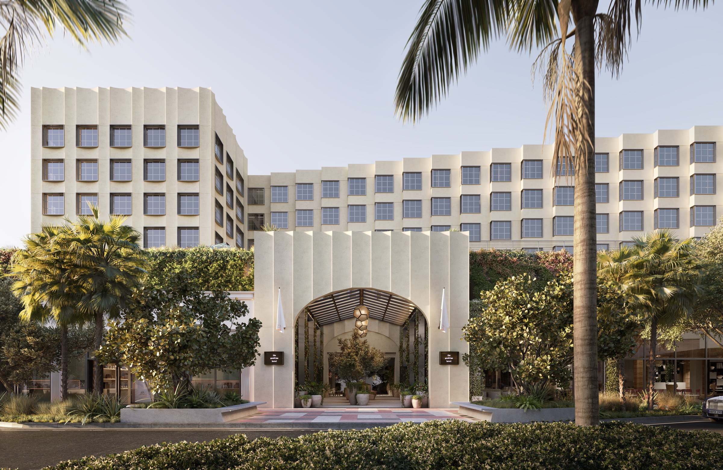 view of front of hotel building with a large arched hall at the front entrance and palm trees in the foreground.