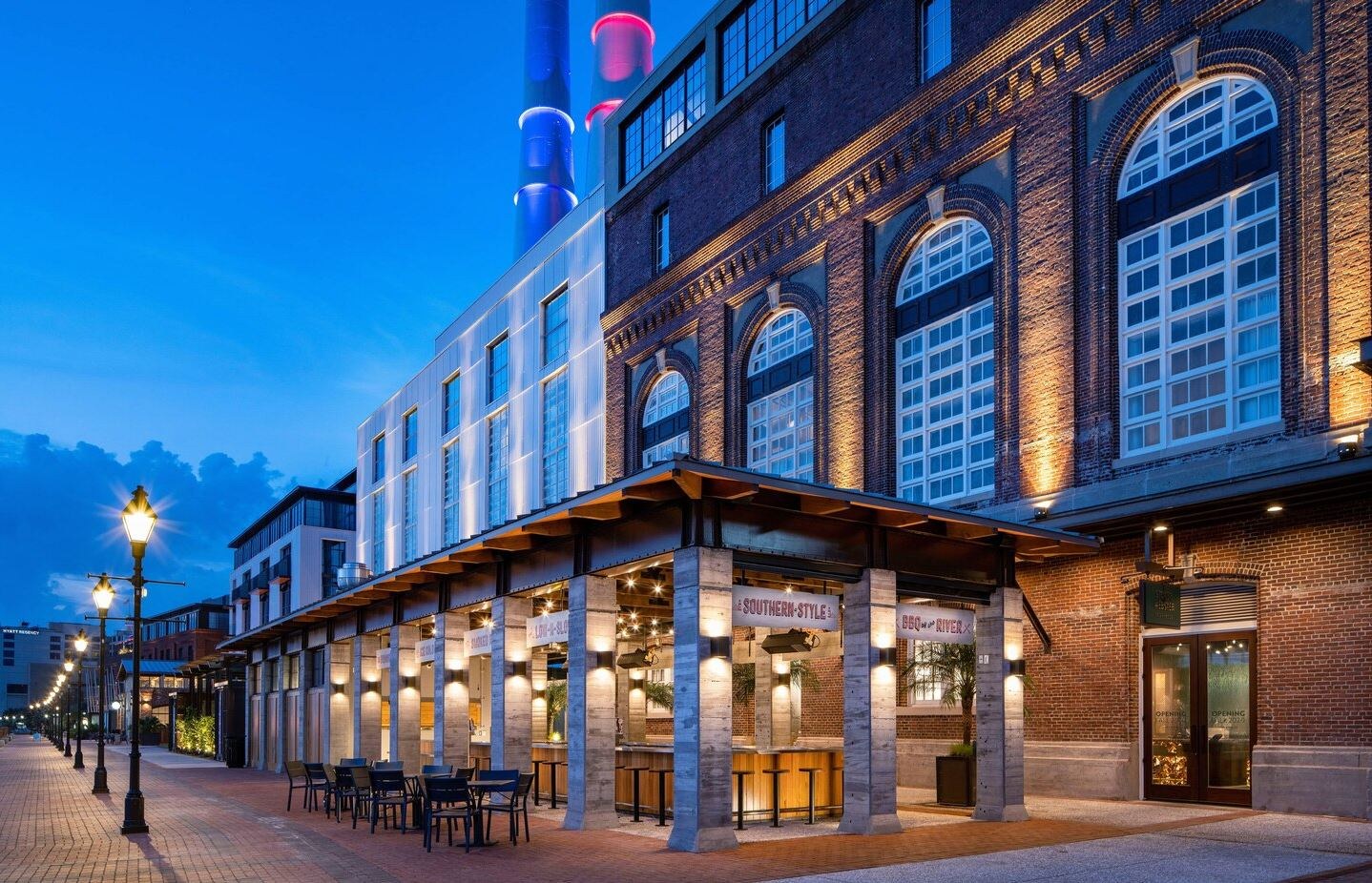 Night photo of renovated, historic power plant with tall windows and stacks in the background.