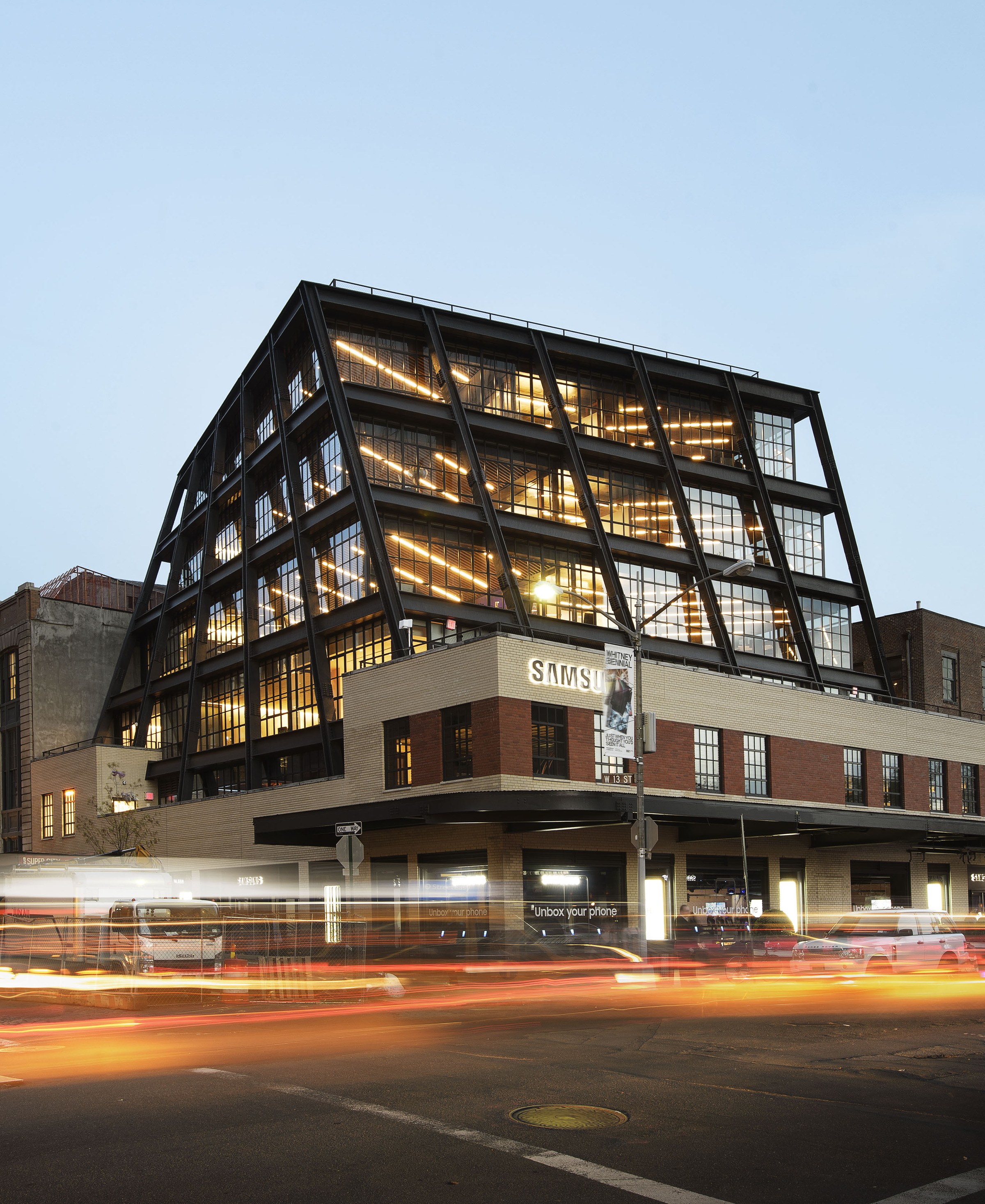 Corner view from a street corner of a modern, 7-story building with large glass windows and exterior steel supports that form a slight vertical twist to the building.