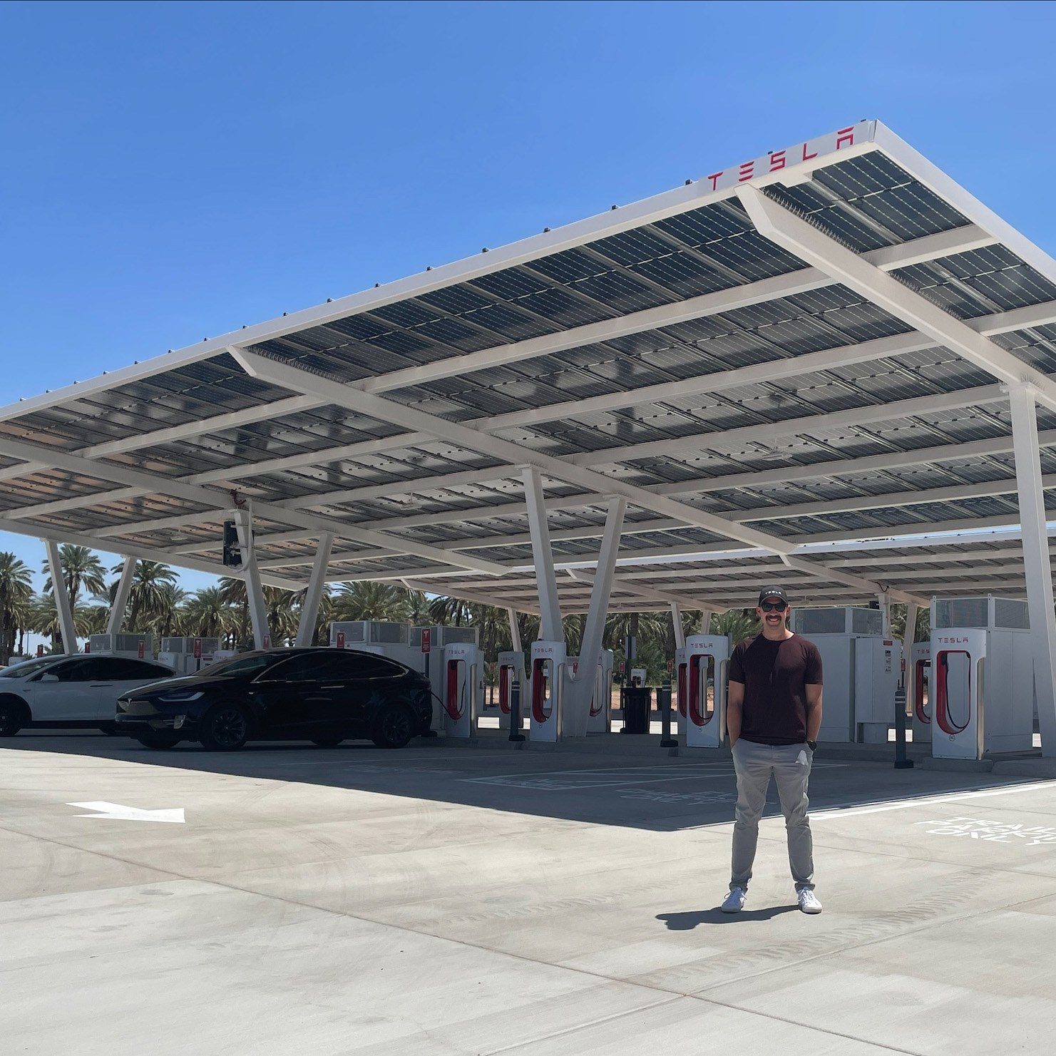 Man standing in front of an outdoor Tesla charging station with canopies overhead used for solar panels.