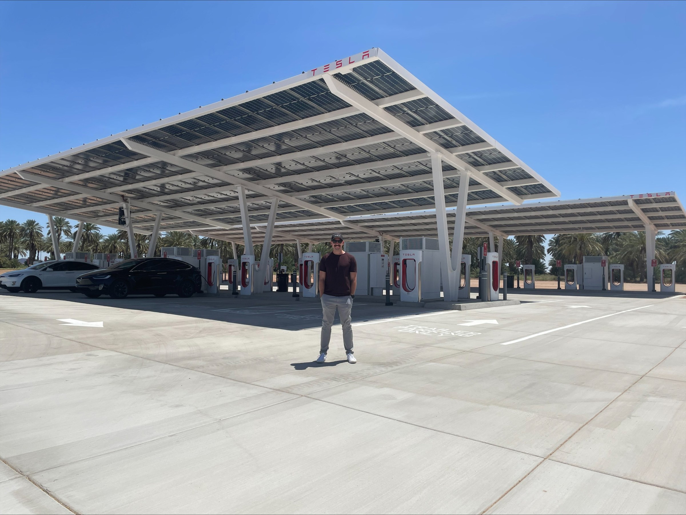 Man standing in front of an outdoor Tesla charging station with canopies overhead used for solar panels.