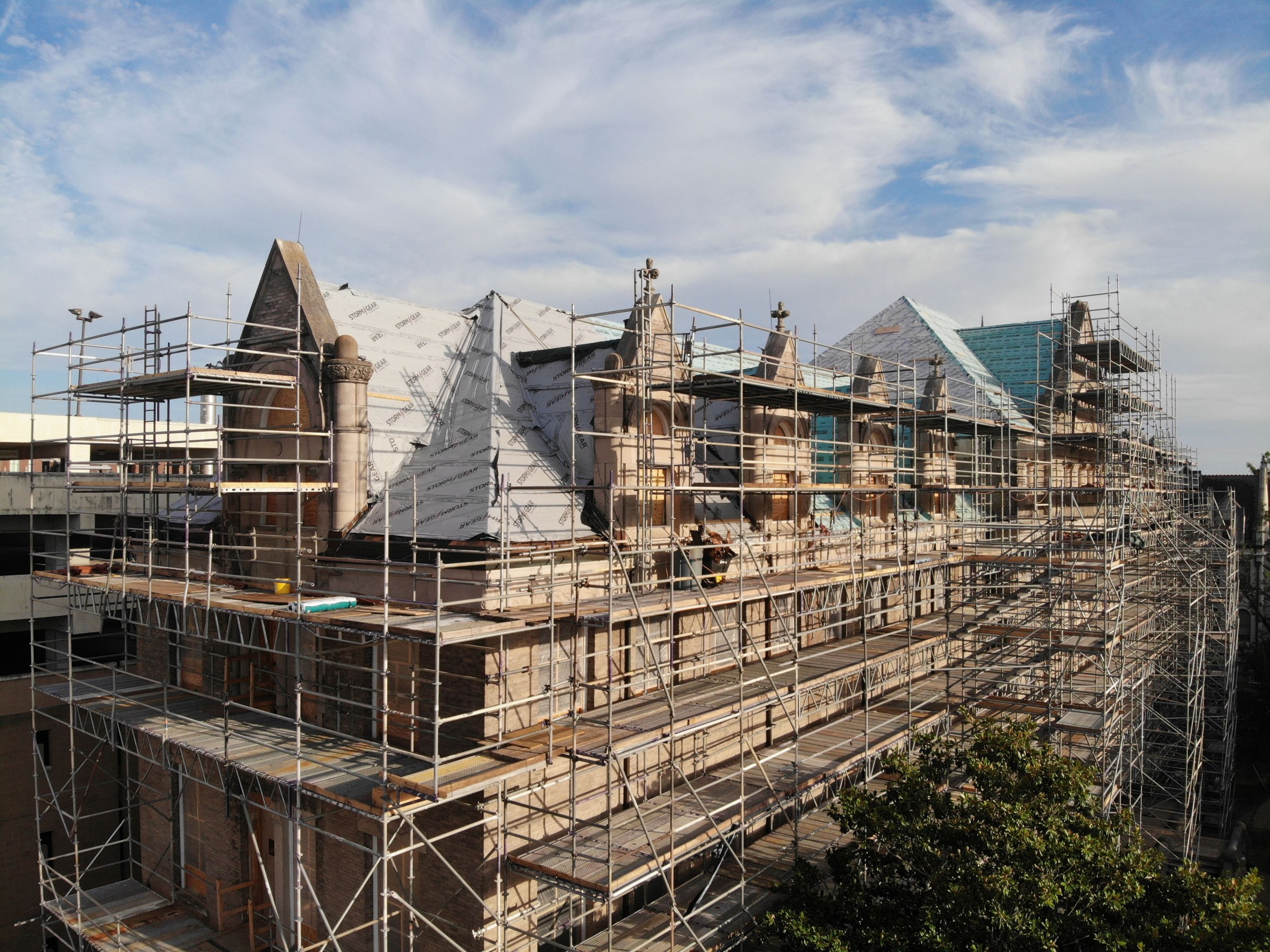 Aerial drone view of the upper northwest corner of Richardson Memorial Hall at sunset and lightly cloudy sky above, with scaffolding across the entire facade and dormers of the building.