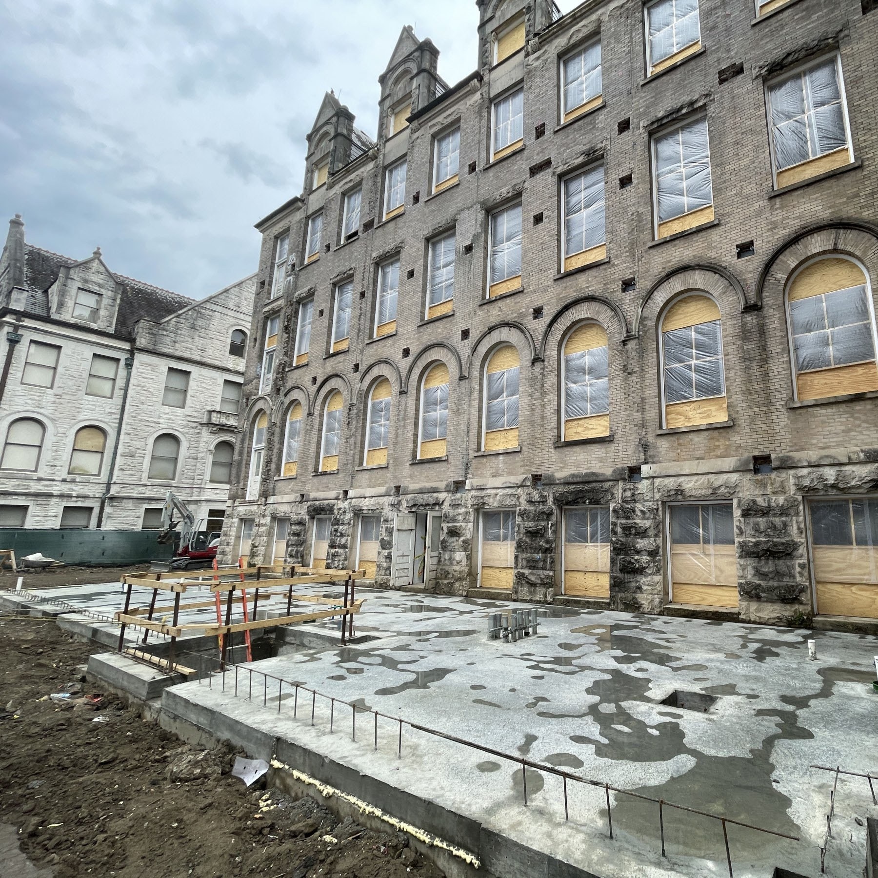 View from the back of a historic limestone building with new slab in foreground, showing that the building will be getting an addition built onto it.