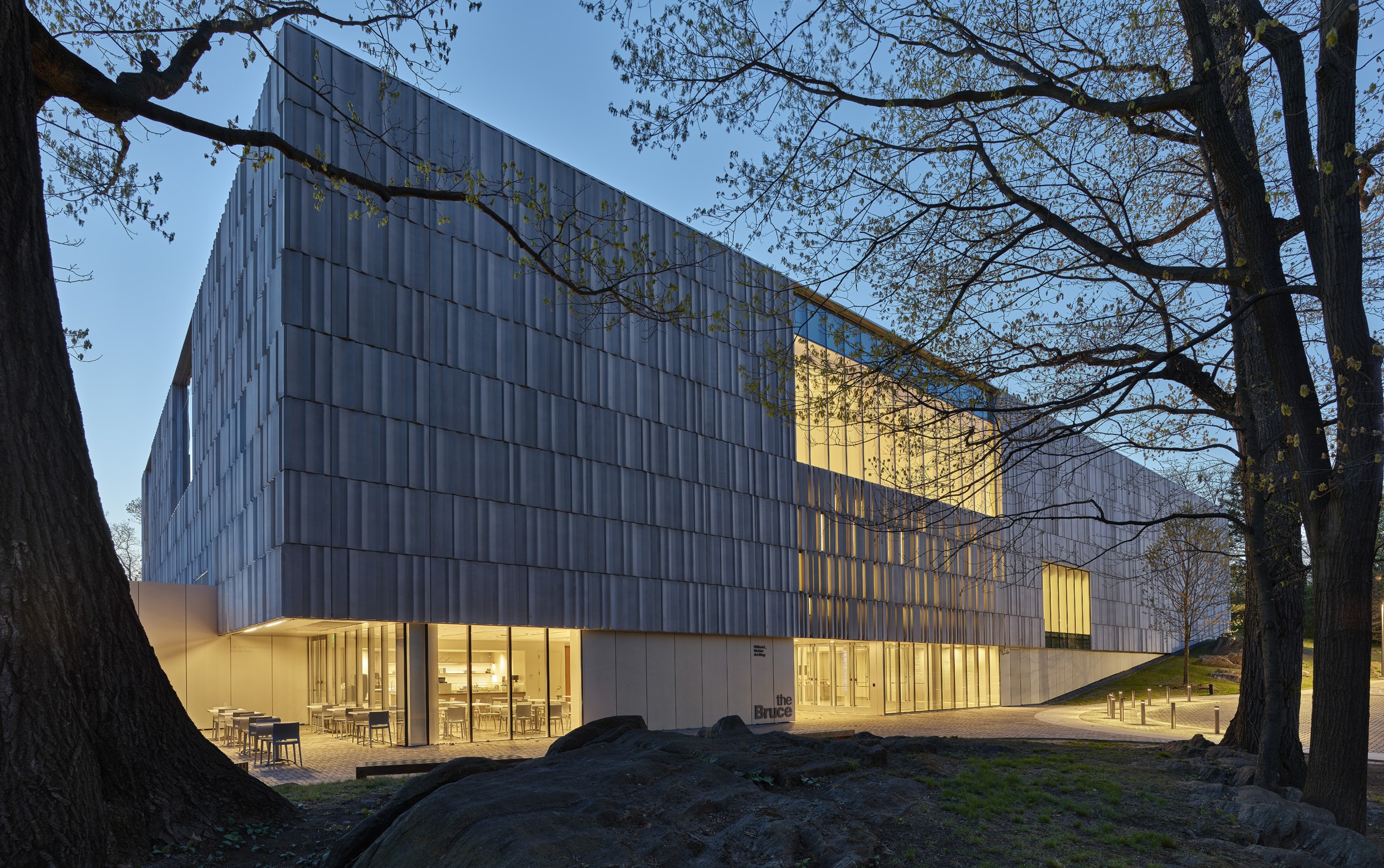 Night photo, looking at the corner of a multi-story museum with some lights on inside, streaming out through screening that wraps around the entire  building.