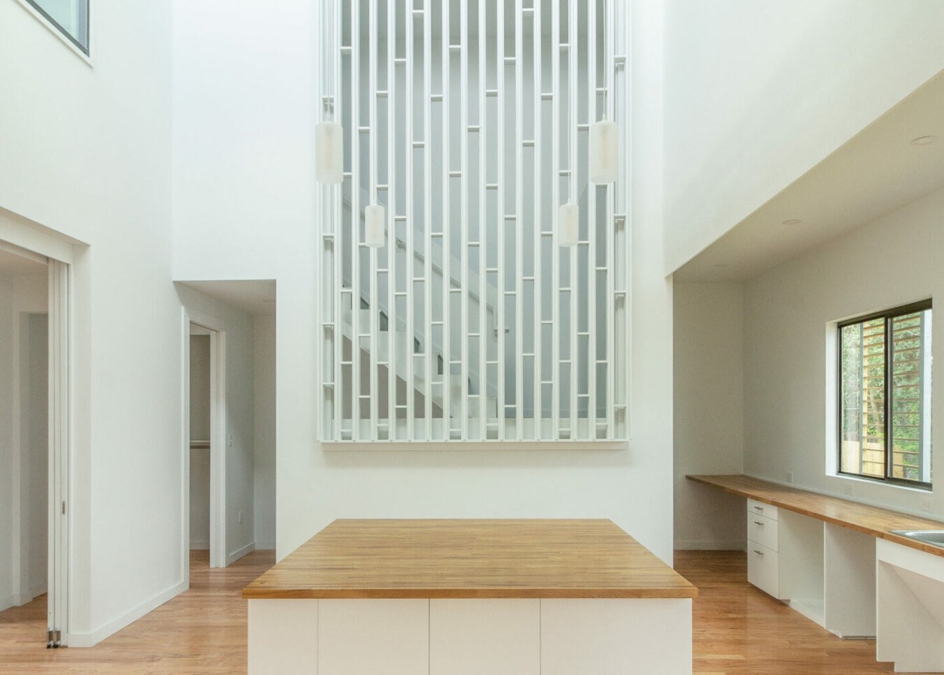 Interior of high-ceiling kitchen space with vertical-slat screen feature built in the foreground with staircase behind the screen