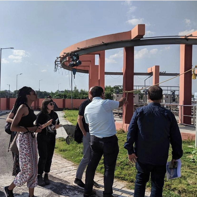 A group of students is shown outdoor equipment at a water-treatment facility in India.