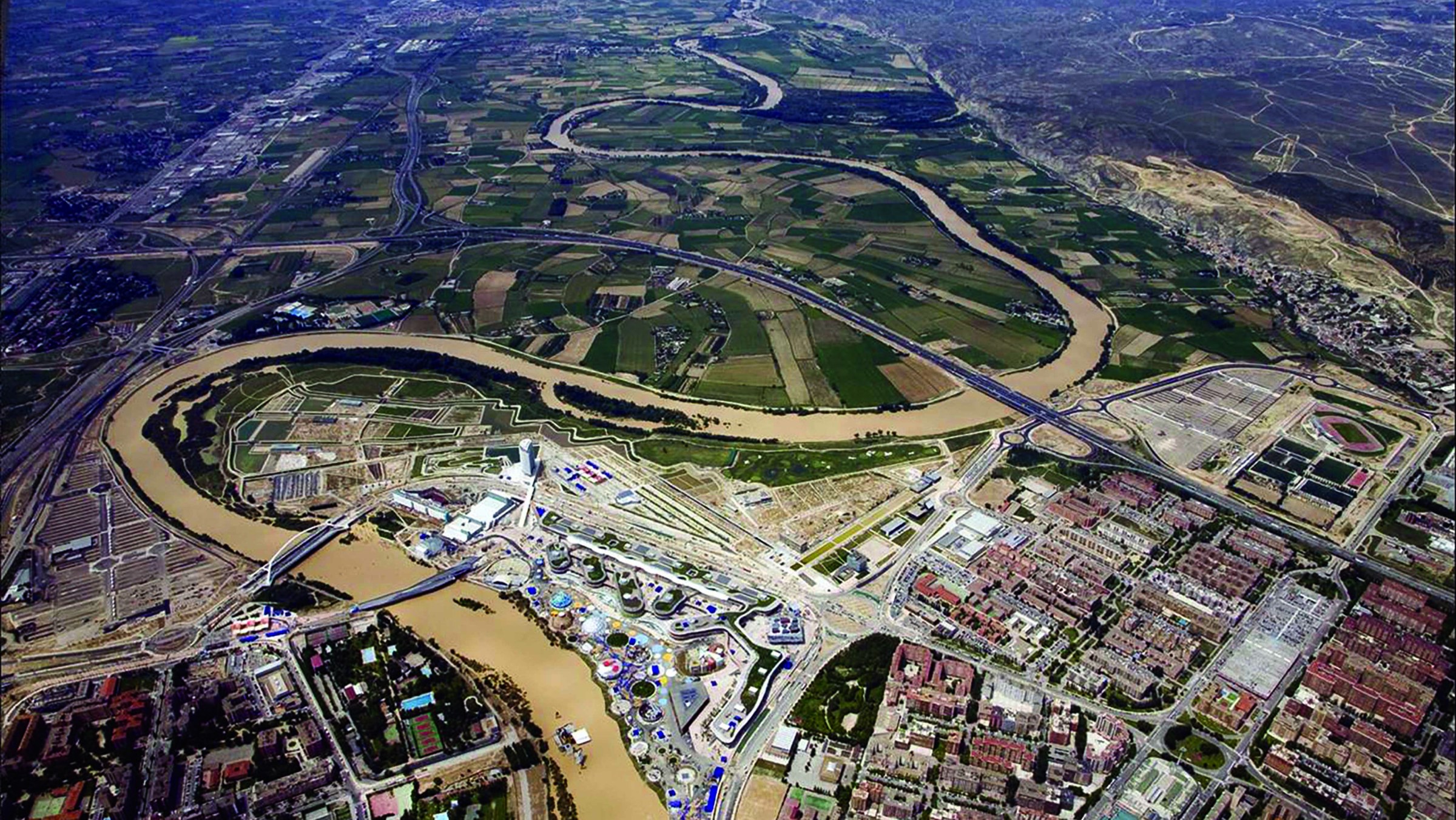 Aerial photo of a winding river through undeveloped and urbanized areas in Zaragoza, Spain.