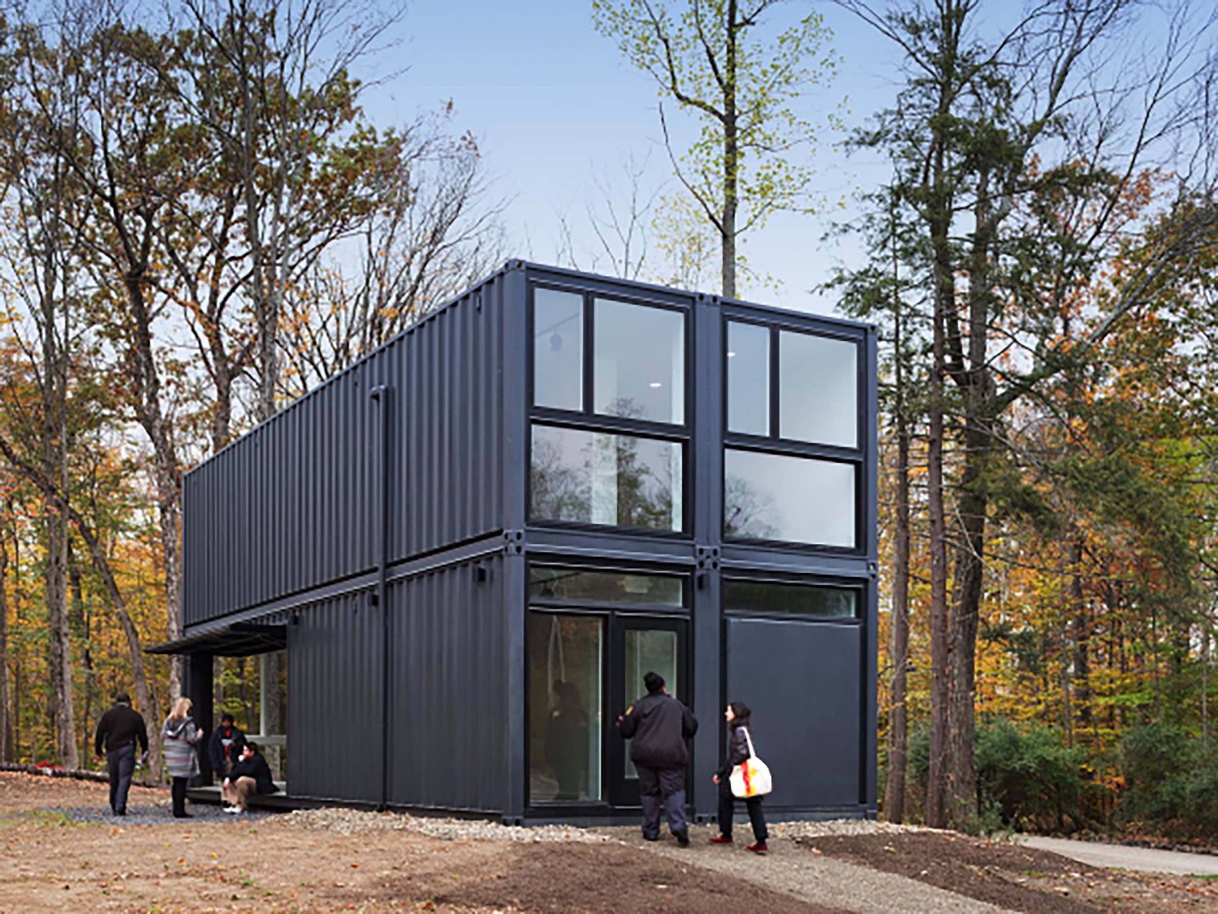 Black revamped, modern shipping container in forest with people around